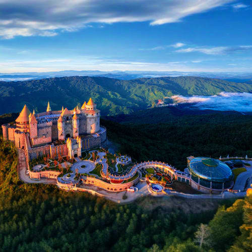 Aerial view of Neuschwanstein Castle nestled in forested Bavarian mountains under blue sky with surrounding landscape