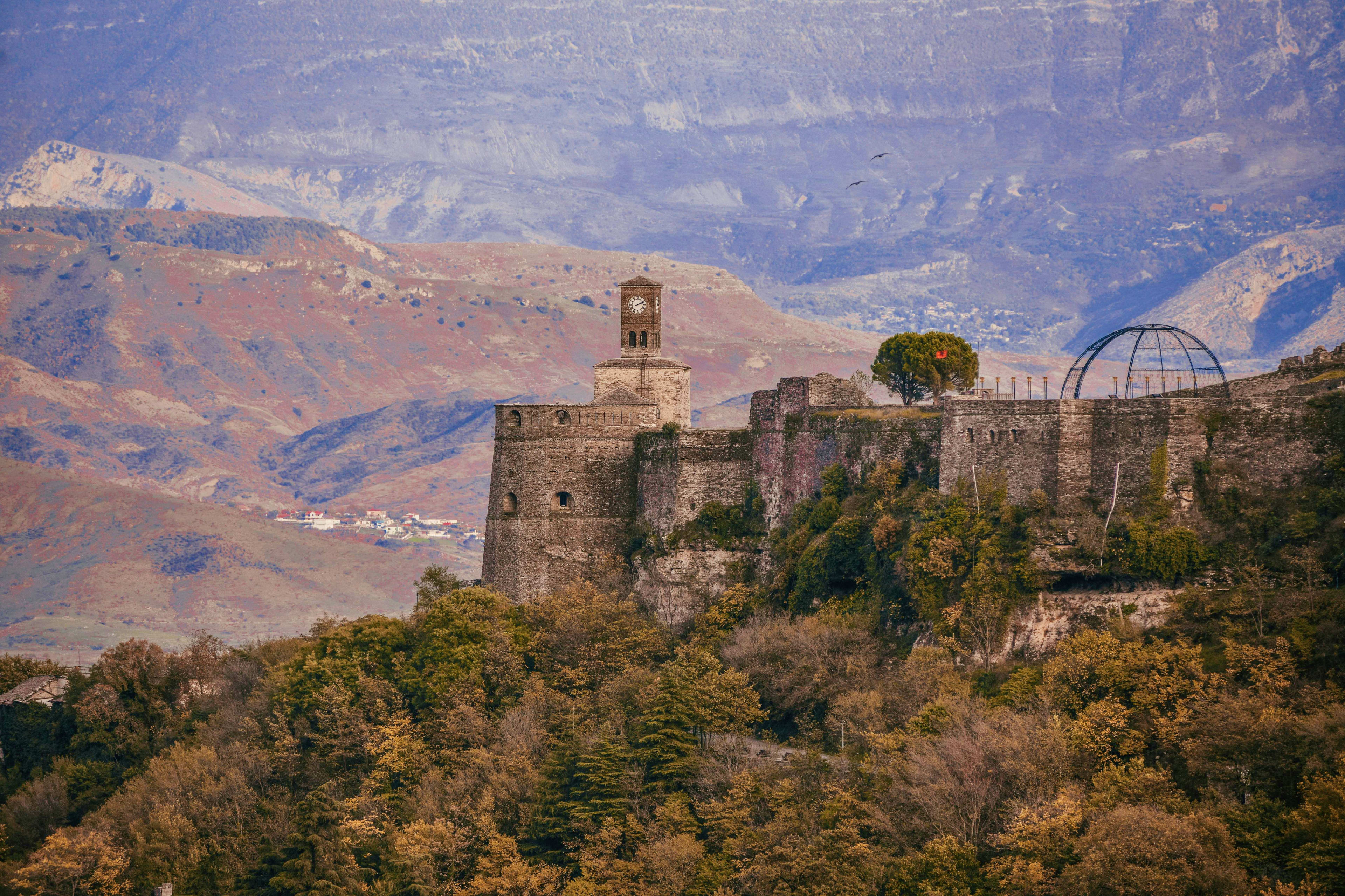 Albania Ancient stone fortress with clock tower overlooking Albanian mountain valley and forested hillside