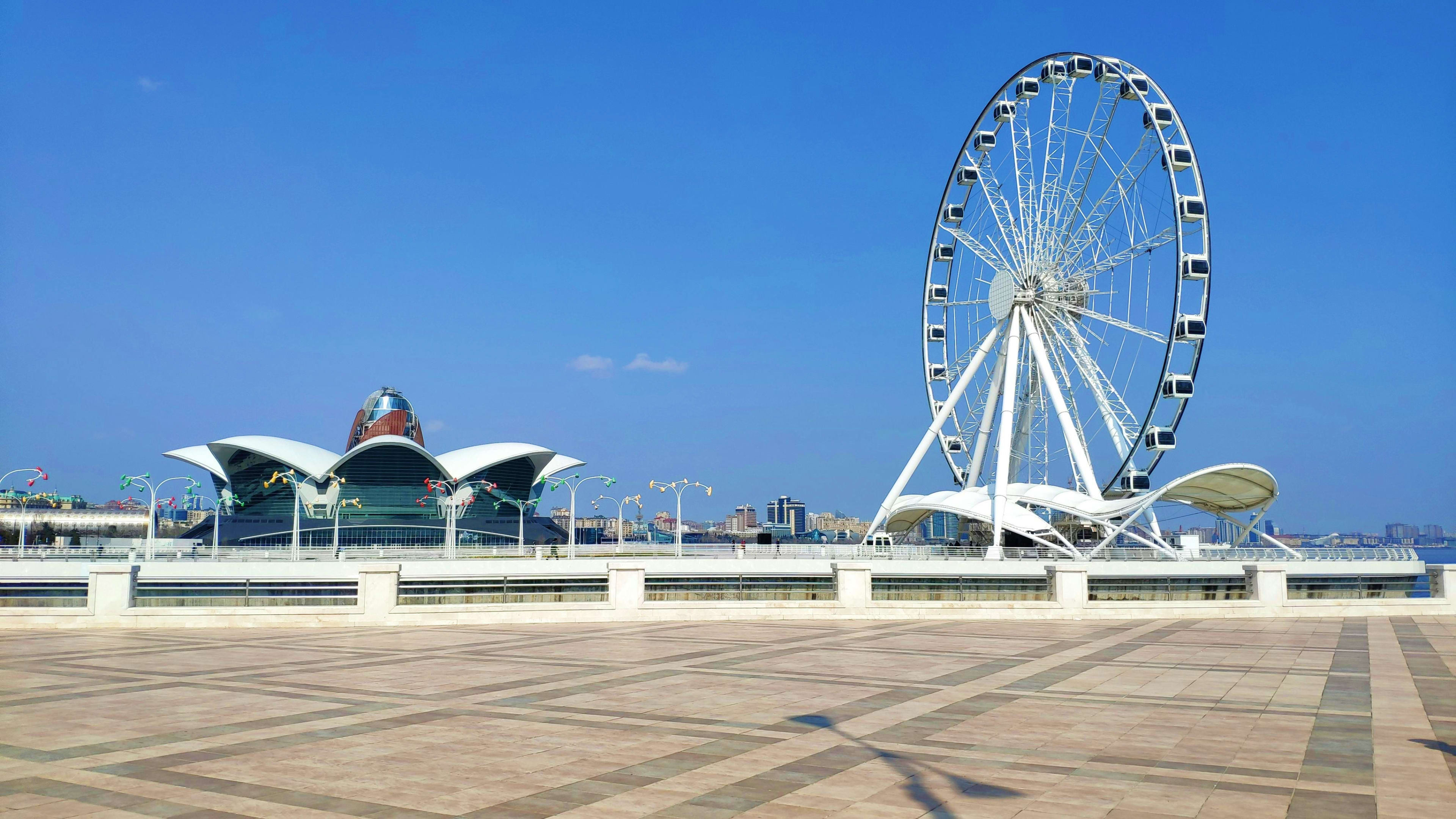 Azerbaijan White Ferris wheel and modern architectural structures on waterfront promenade in Baku, Azerbaijan under blue sky