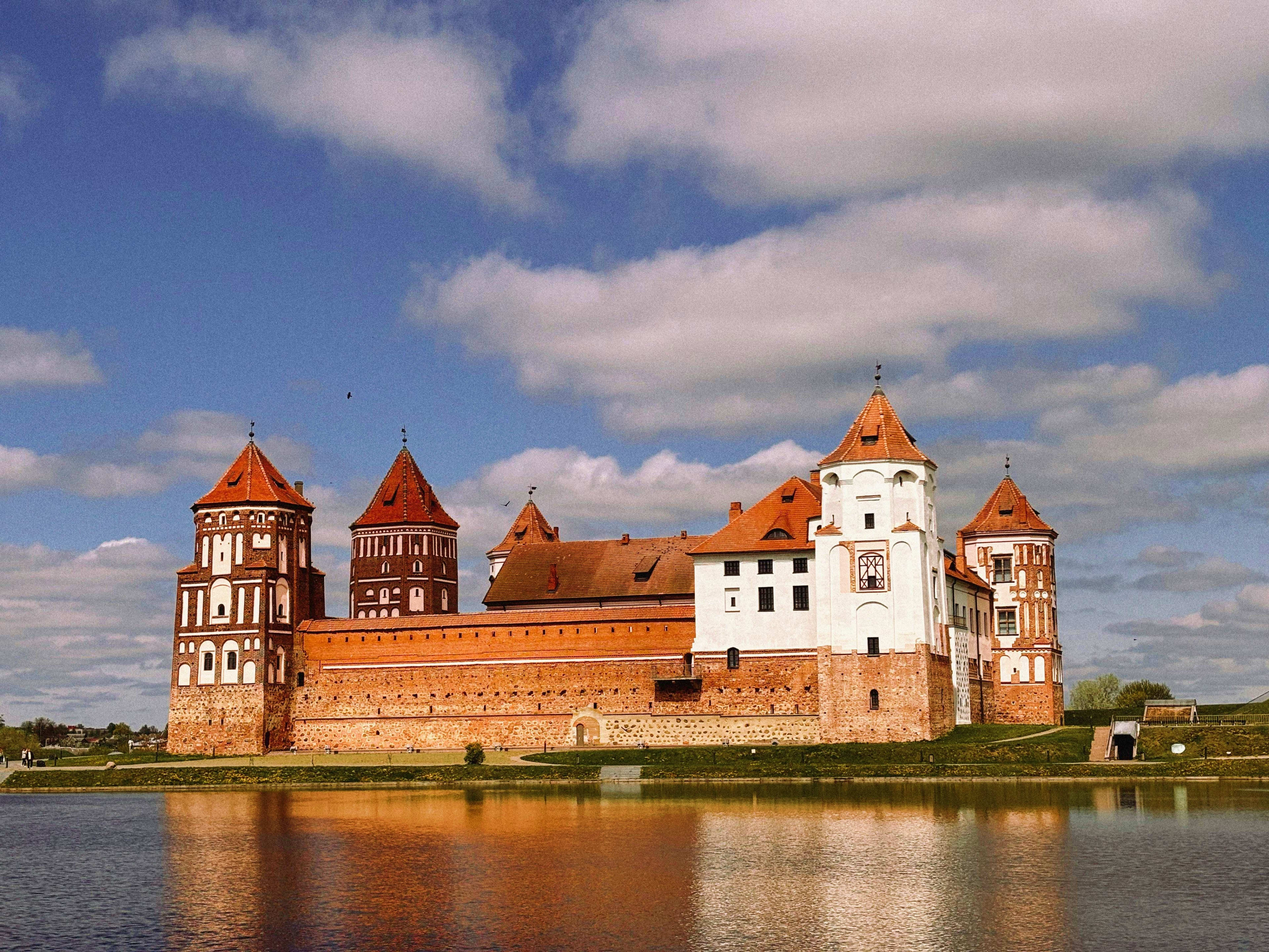 Belarus Mir Castle reflected in water, medieval fortress with red-tiled towers and white central keep in Belarus