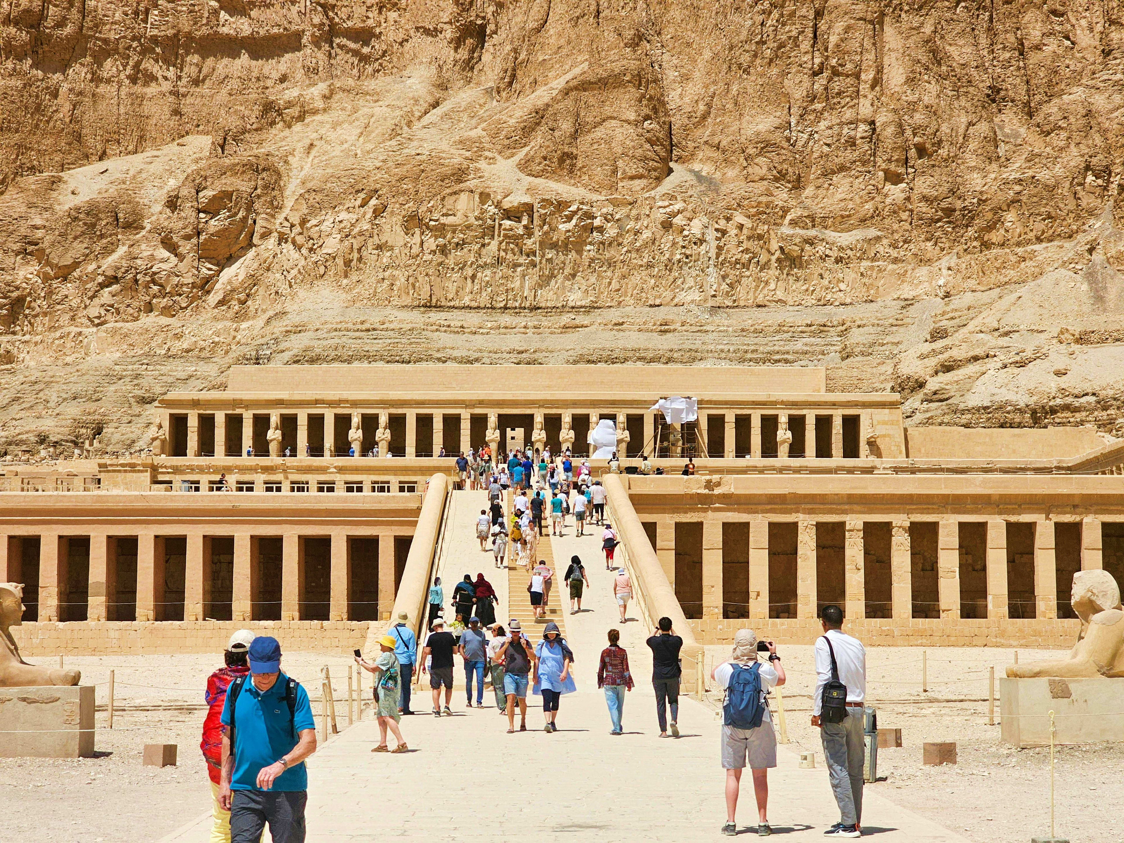 Egypt Tourists walking toward the Temple of Hatshepsut in Egypt, with massive columned facade carved into limestone cliffs