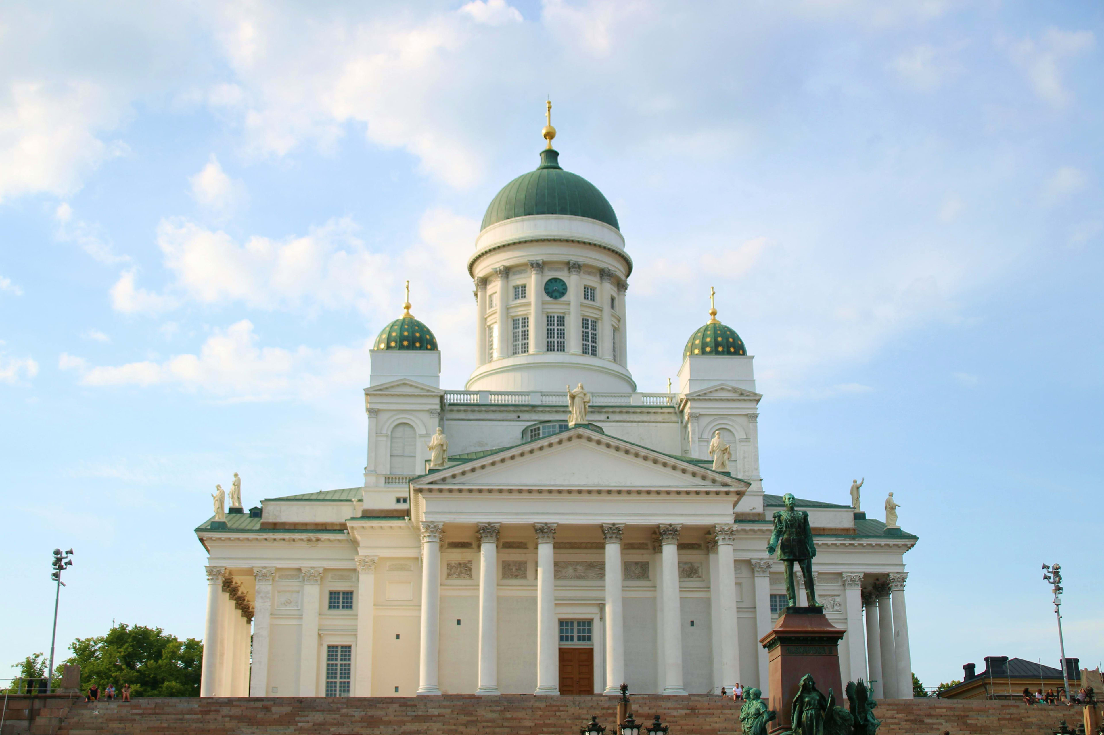 Finland Helsinki Cathedral with white neoclassical facade, green domes, and gold crosses against blue sky with clouds