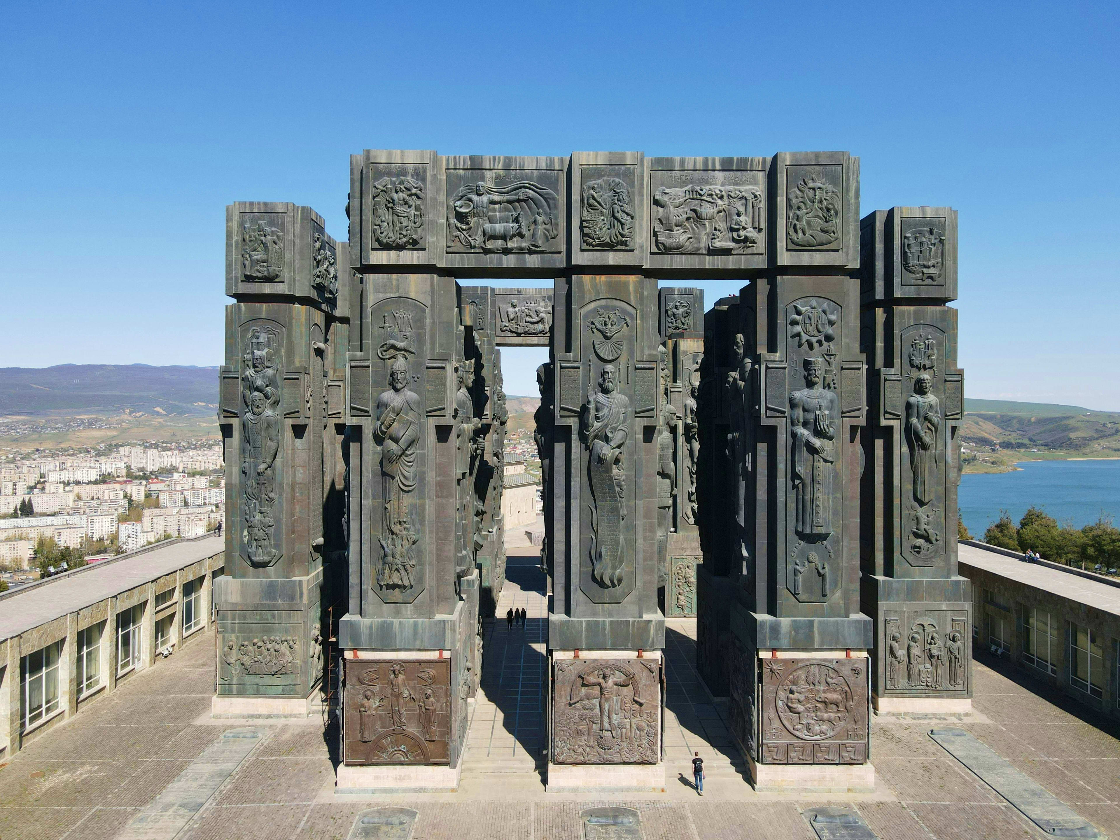 Georgia Stone monument with ornate carved reliefs depicting figures and mythological scenes, overlooking Georgian city and lake lands