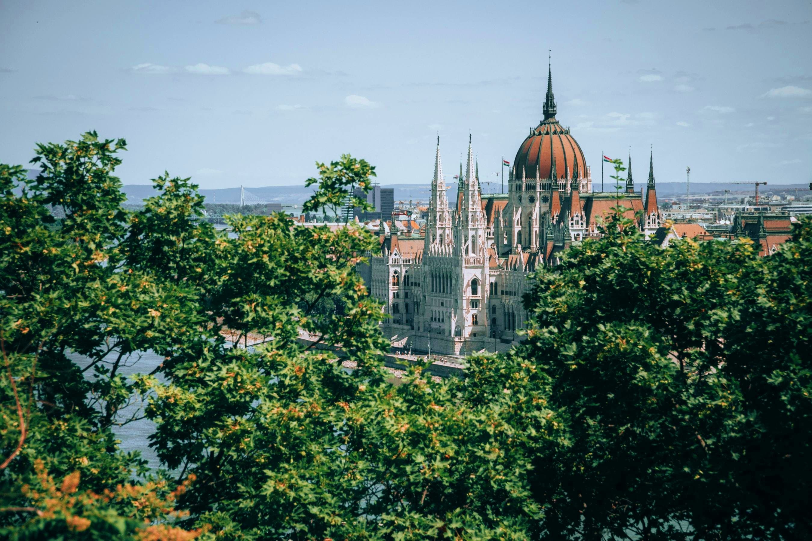 Hungary Hungarian Parliament Building with copper dome and Gothic spires viewed through green foliage, Danube River in background
