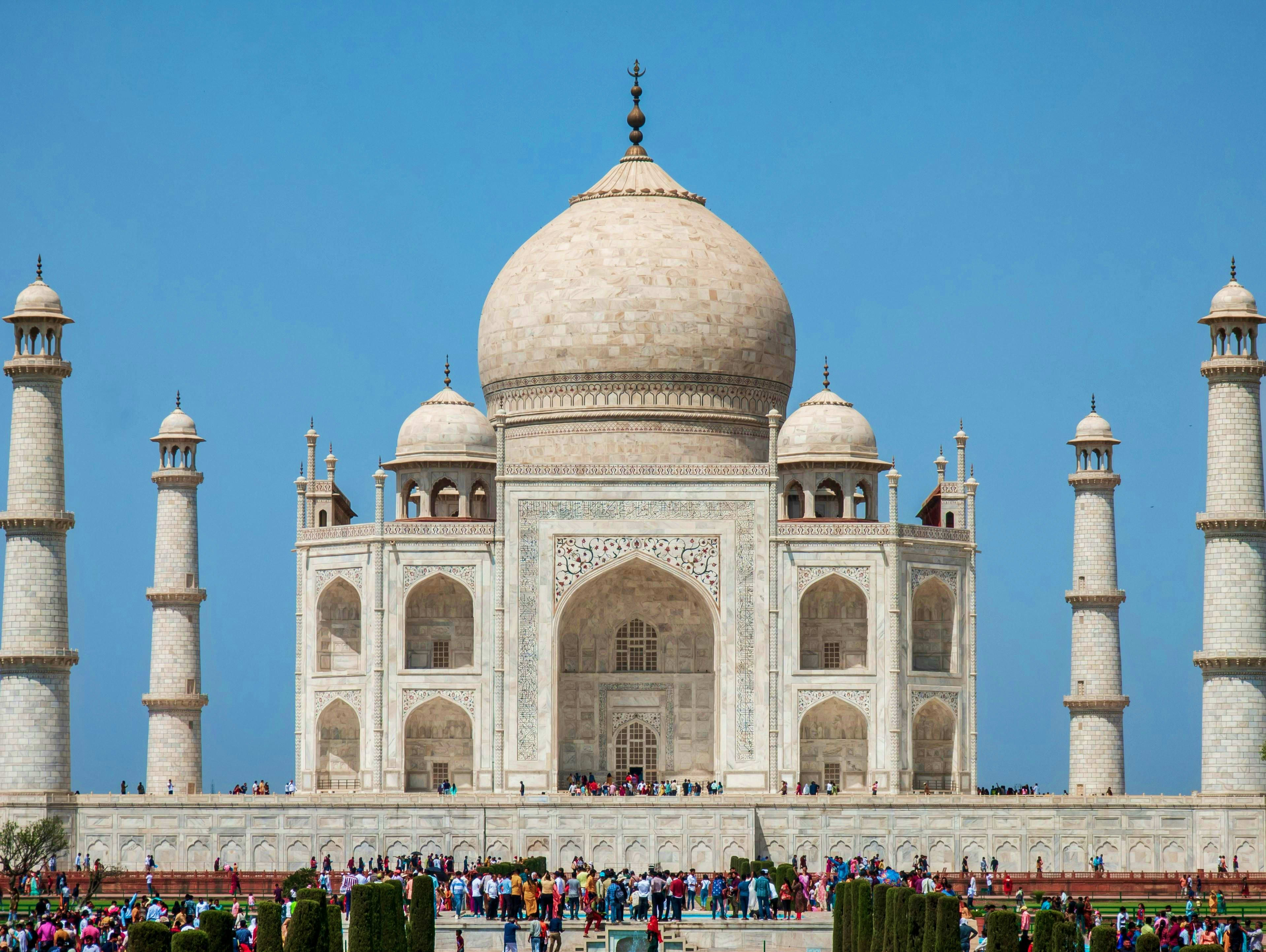 India Taj Mahal front facade with domes and minarets against clear blue sky with tourists gathered in courtyard