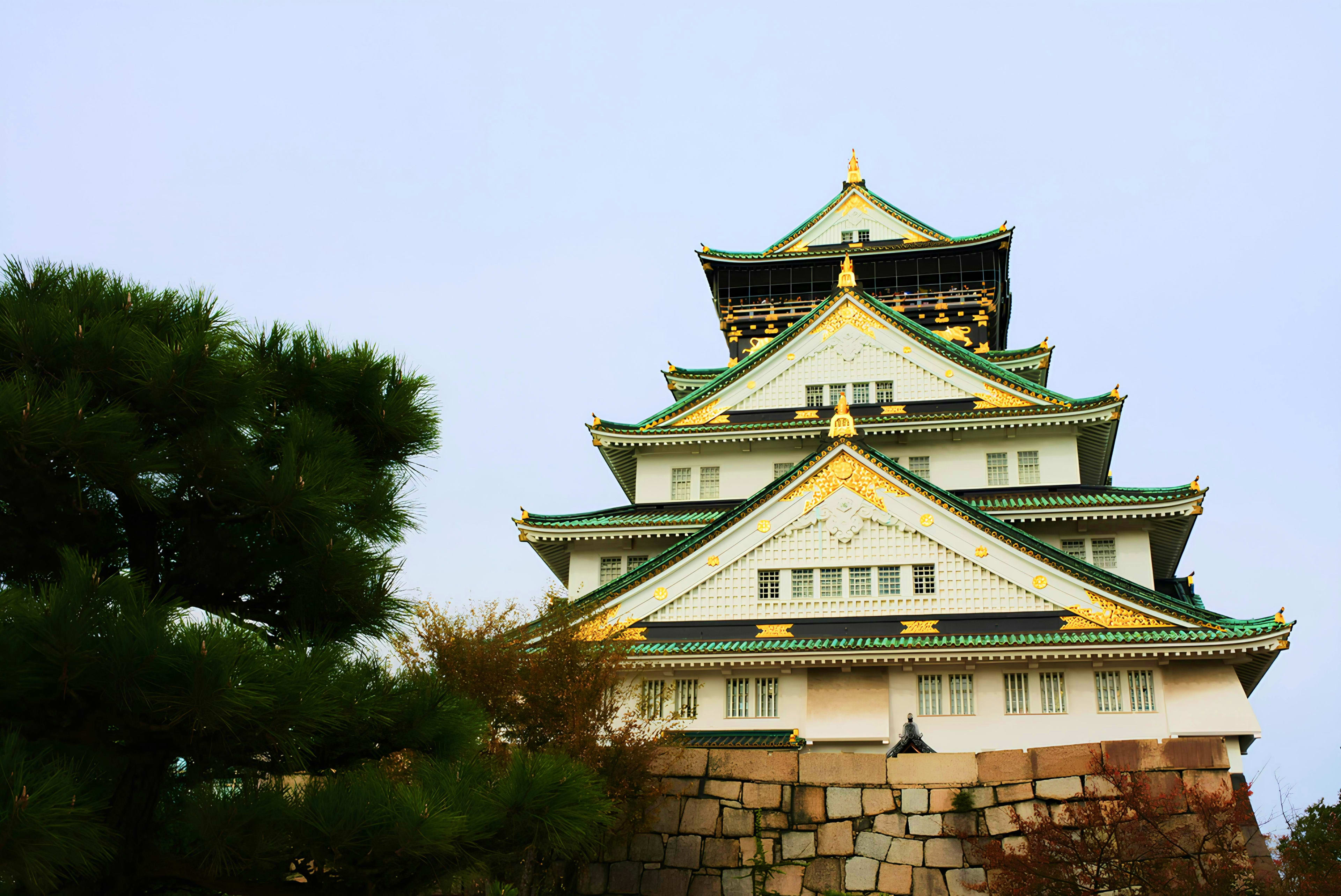 Japan Osaka Castle with distinctive tiered roofs featuring green glazed tiles and gold ornaments, surrounded by palm trees against