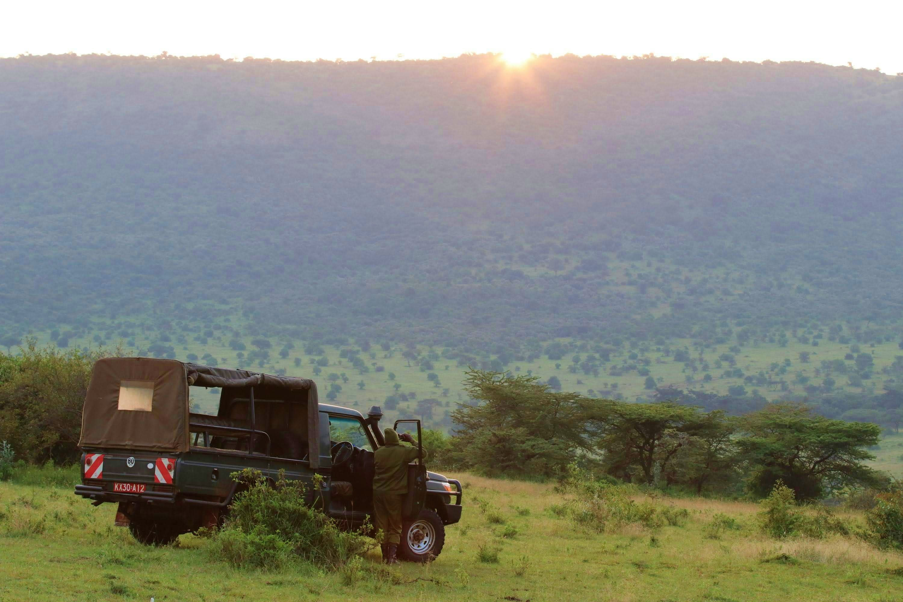 Kenya Safari vehicle parked on grassland overlooking vast valley at sunrise in Kenya
