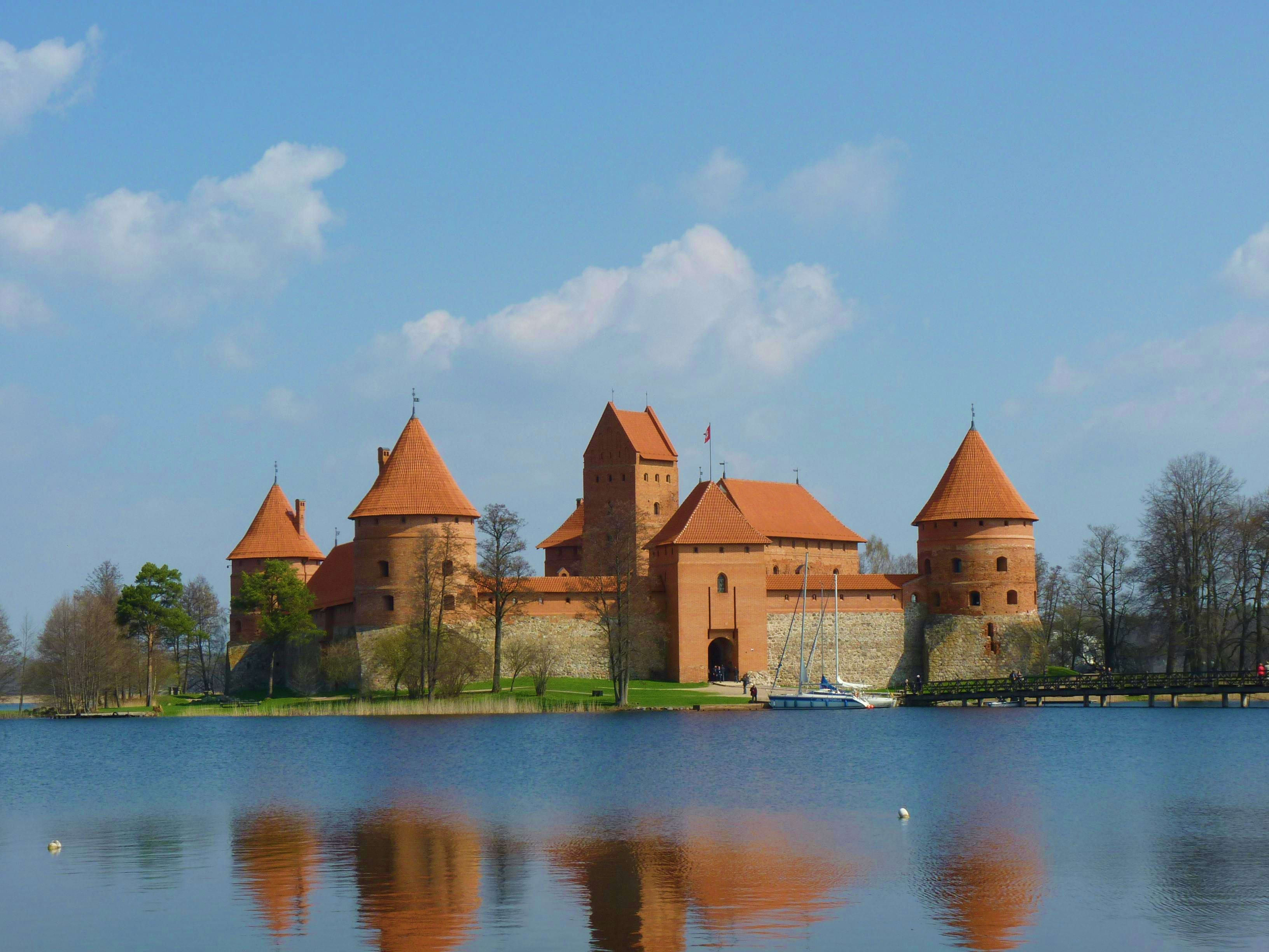 Lithuania Trakai Island Castle reflected in water, featuring distinctive red-brick towers under blue sky in Lithuania