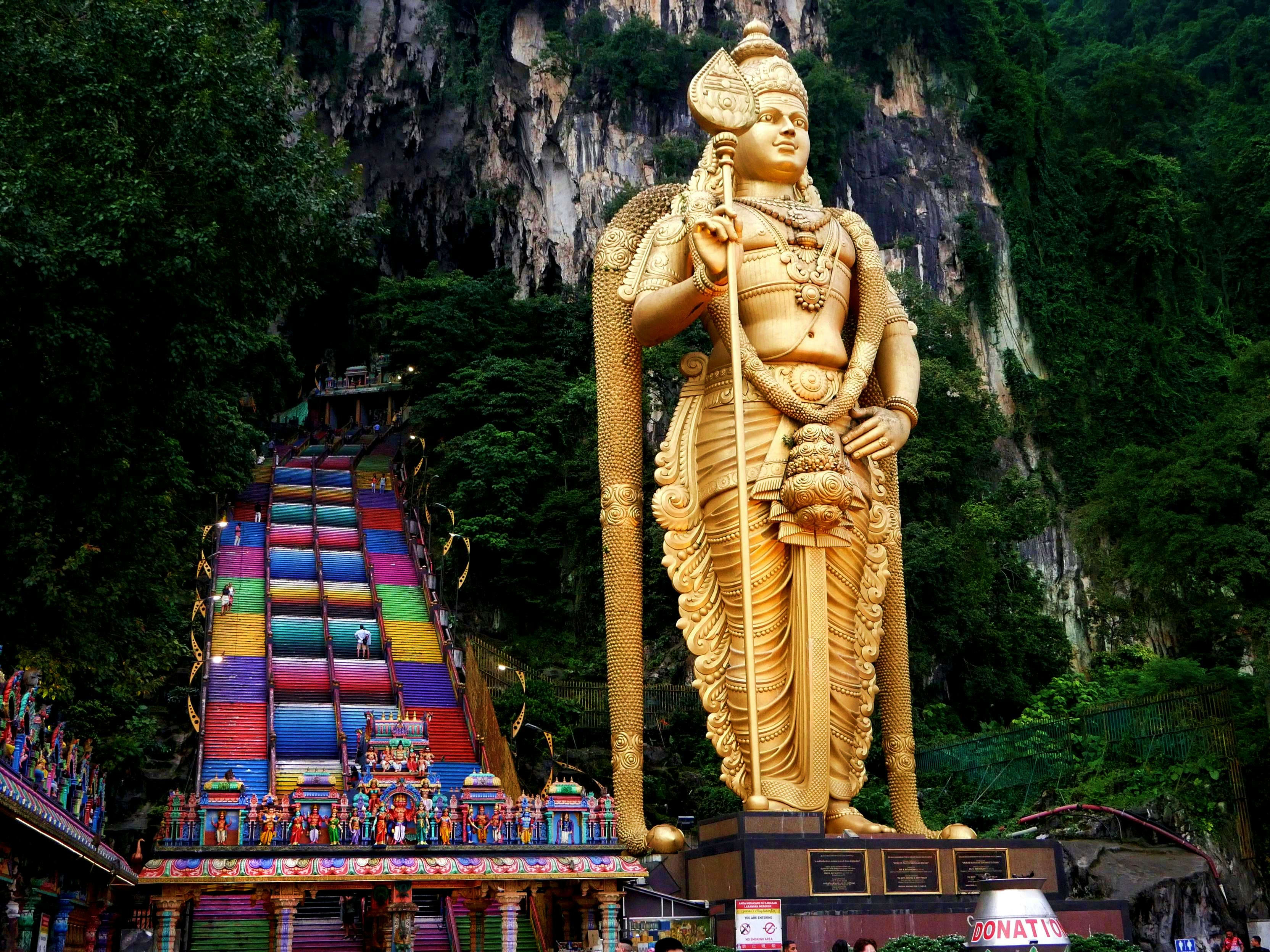 Malaysia Giant golden statue of Lord Murugan at Batu Caves with colorful rainbow staircase and limestone cliffs in Malaysia