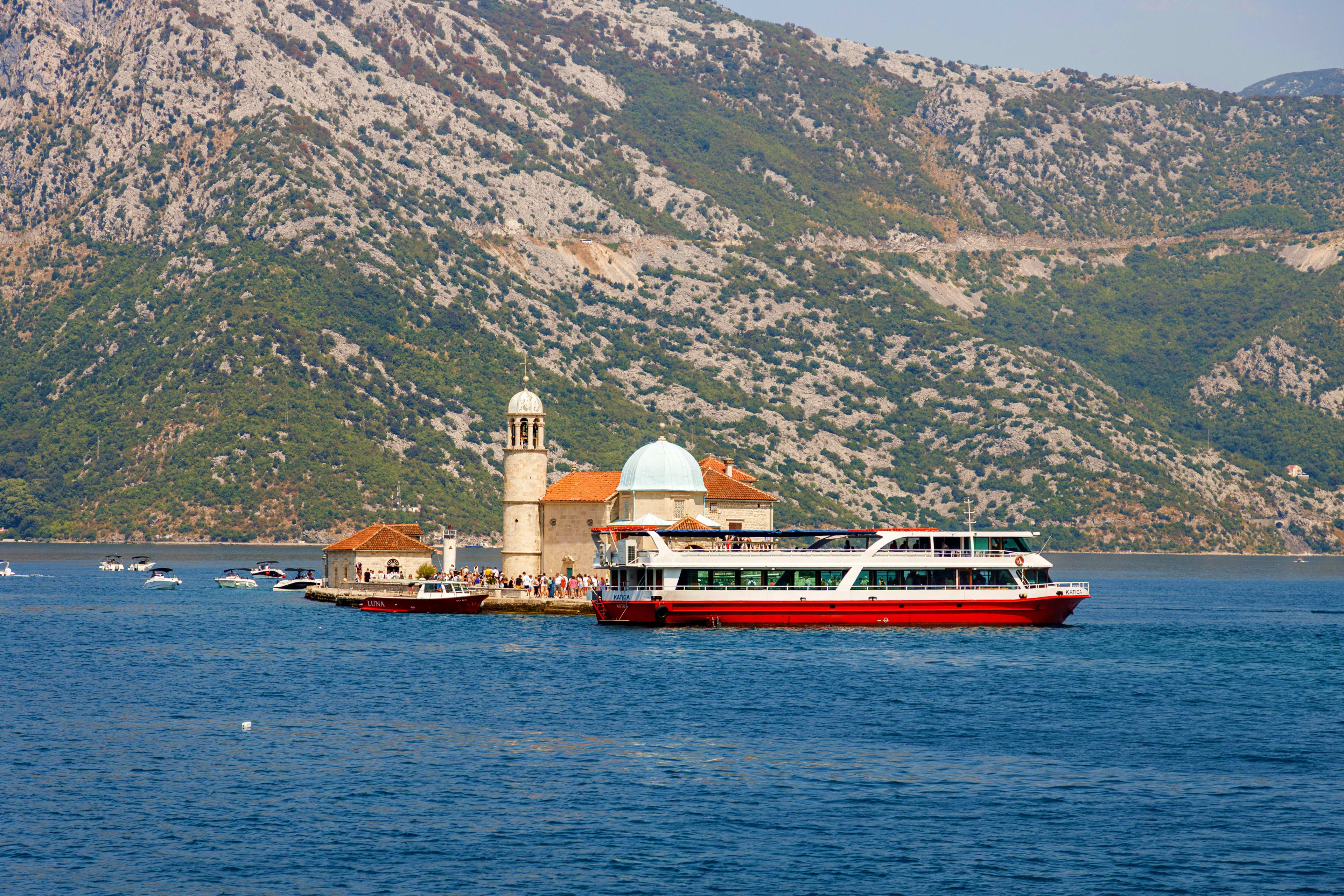 Montenegro Kotor Bay coastal landscape with historic mosque featuring white dome and minaret, red and white passenger ferry boat, limest