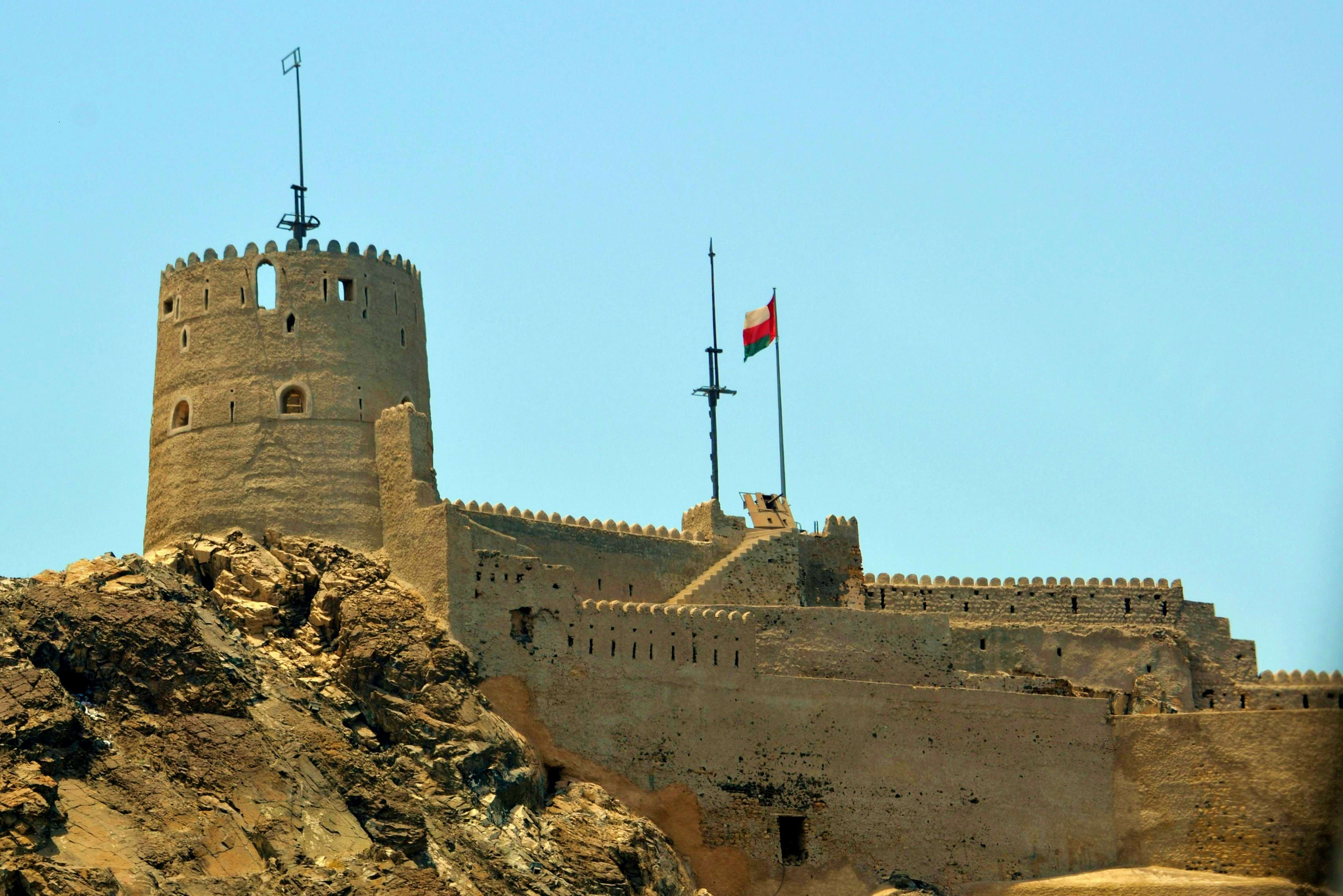 Oman Ancient stone fortress with crenellated walls and towers overlooking rocky terrain under clear blue sky in Oman