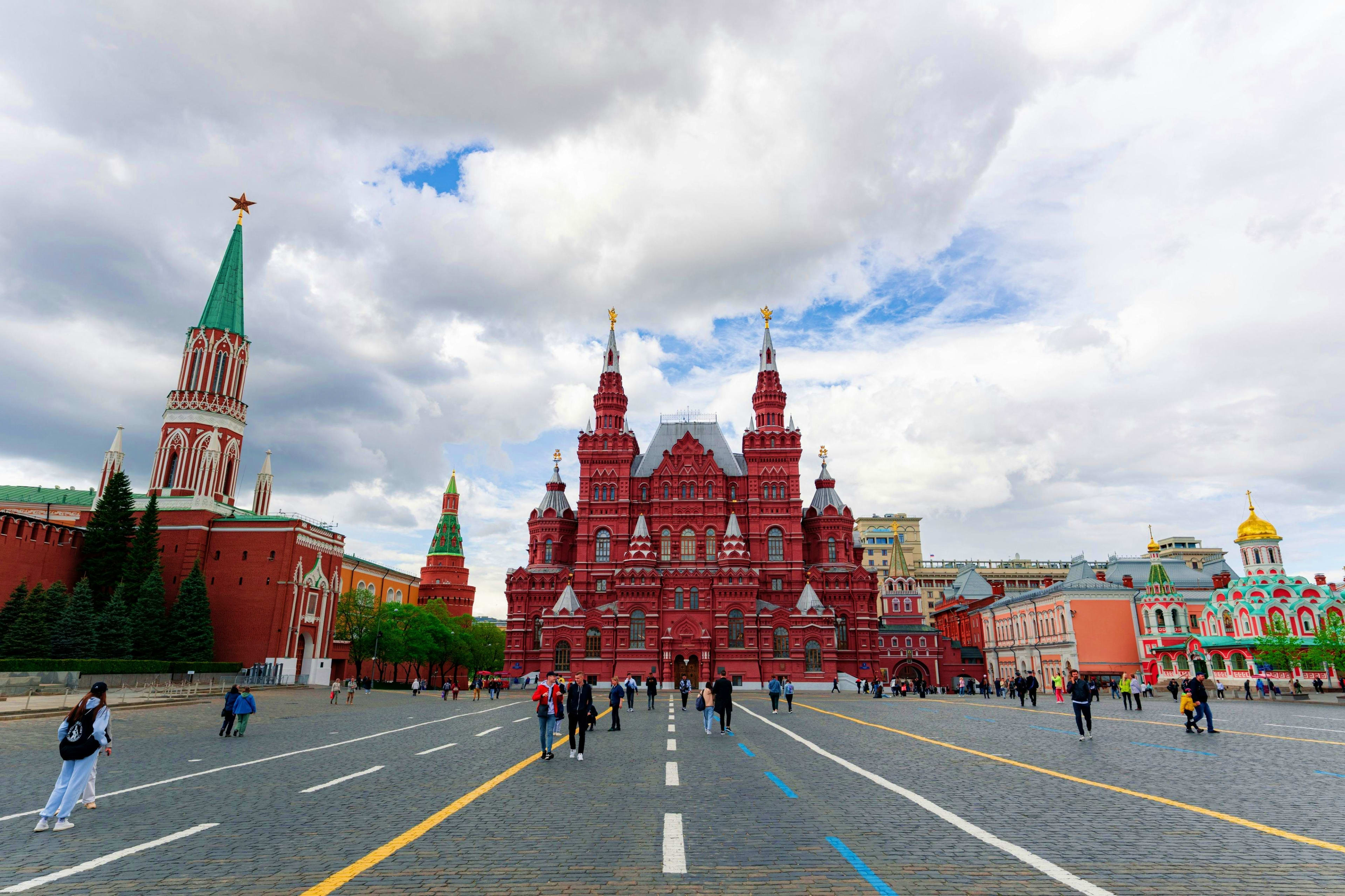 Russia Red Square in Moscow with State Historical Museum and Kremlin tower under cloudy sky, tourists walking on brick plaza