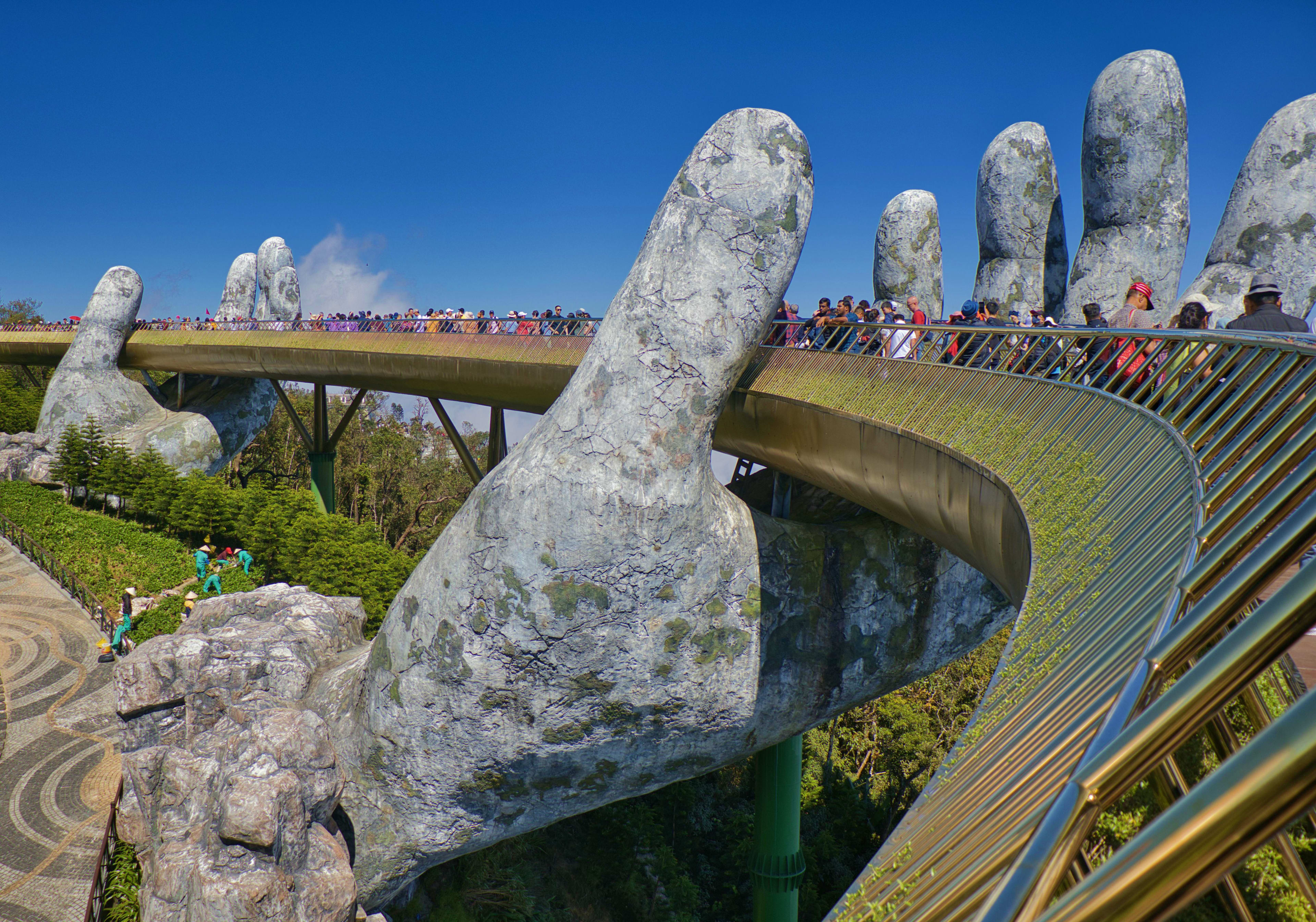 Vietnam Giant stone hands supporting a curved bridge with tourists walking across, Golden Bridge in Da Nang, Vietnam