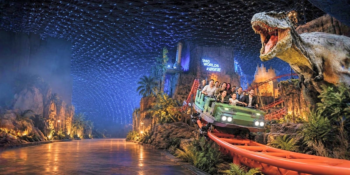 Adventure ride vehicle with passengers traversing through dinosaur-themed jungle landscape with glowing cavern ceiling at IMG