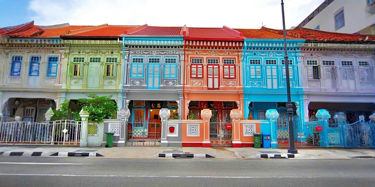 Colorful traditional shophouses in Penang with white, green, orange and blue facades and red tile roofs along a street