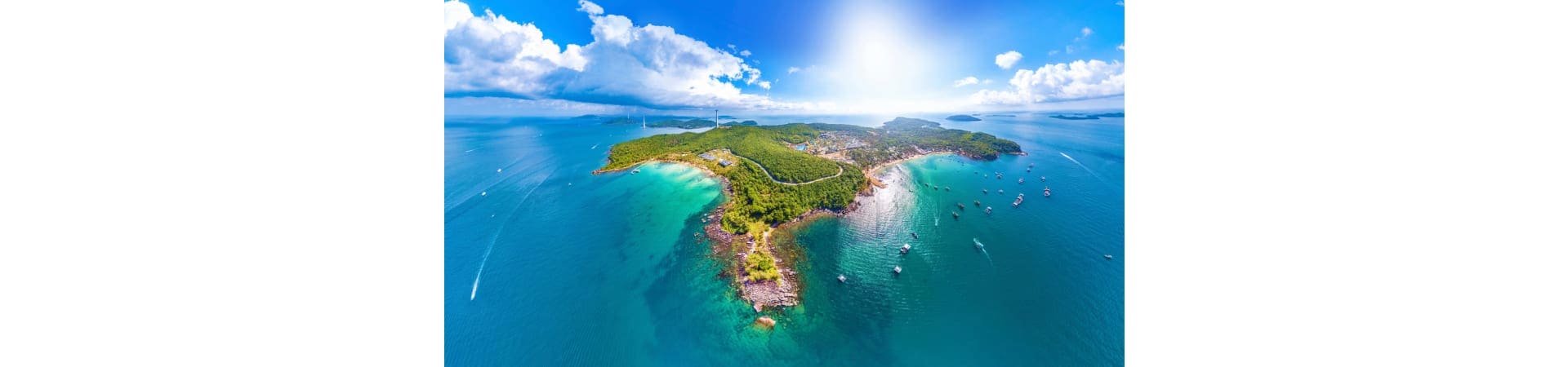 Aerial view of Phu Quoc island with turquoise waters, sandy beaches, forested hills, and moored boats under blue sky
