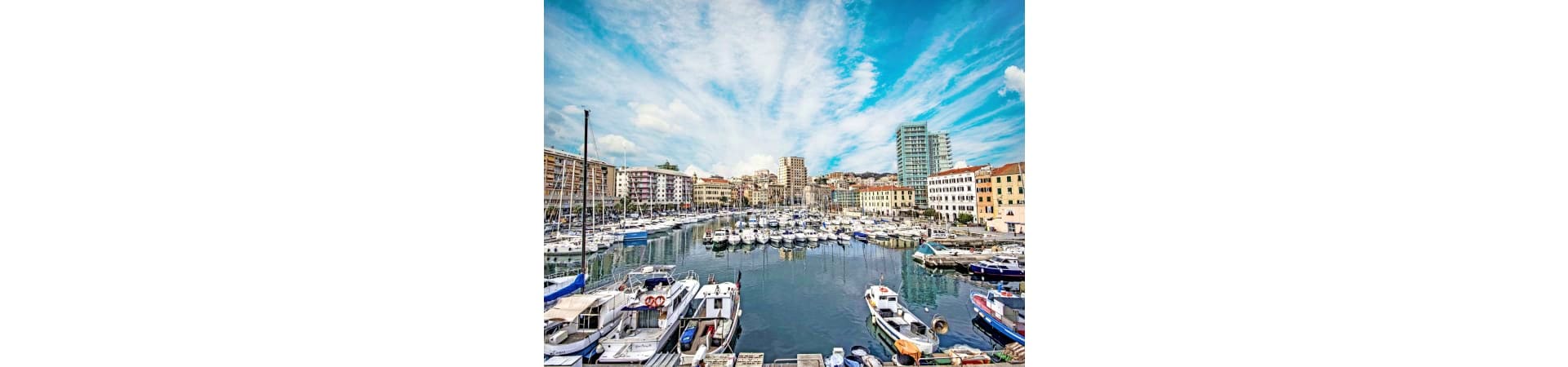 Savona harbor with moored white boats, colorful waterfront buildings, and blue sky with wispy clouds