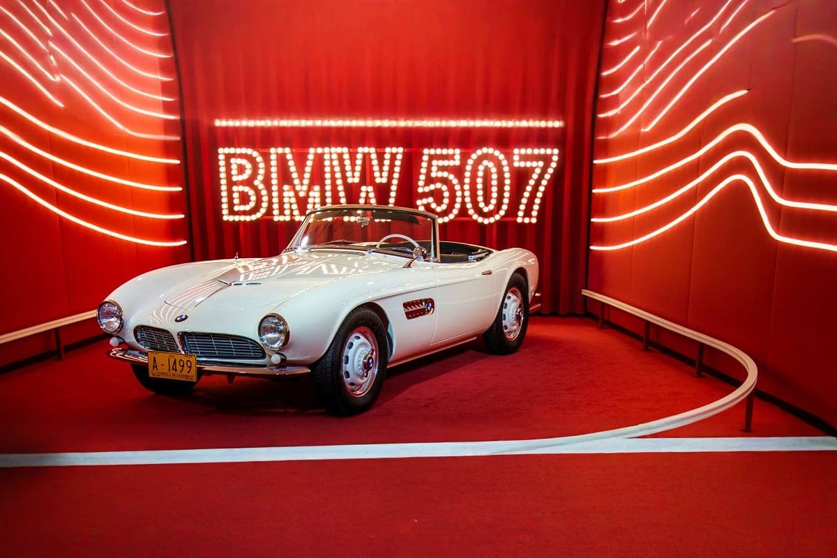 White BMW 507 classic convertible displayed on red platform with illuminated neon sign at BMW Museum