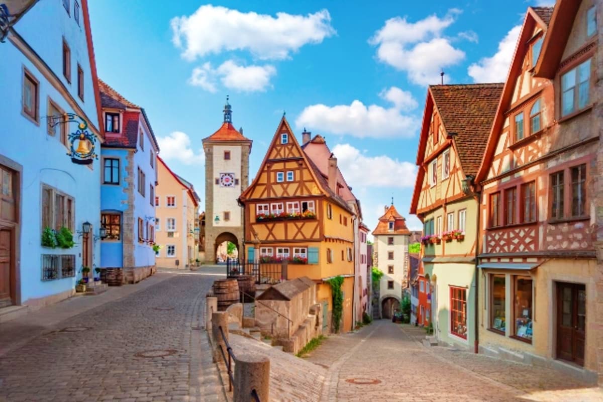 Munich to Neuschwanstein Castle Full Day Tour Historic medieval town street with half-timbered buildings, clock tower, and cobblestone plaza under blue sky