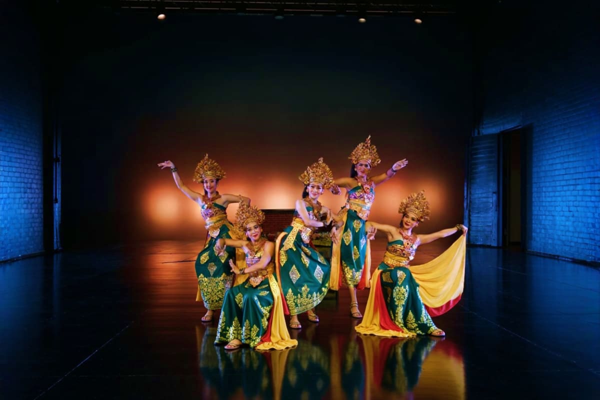 Devdan Show Thai classical dancers in traditional gold headdresses and green silk costumes performing on stage with dramatic orange and b