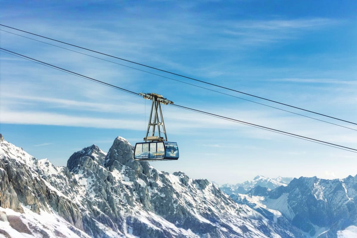 Zugspitze Mountain and Garmisch Day Tour from Munich Cable car ascending to Zugspitze mountain peak with snow-covered Alpine peaks and valley visible below under blue sky
