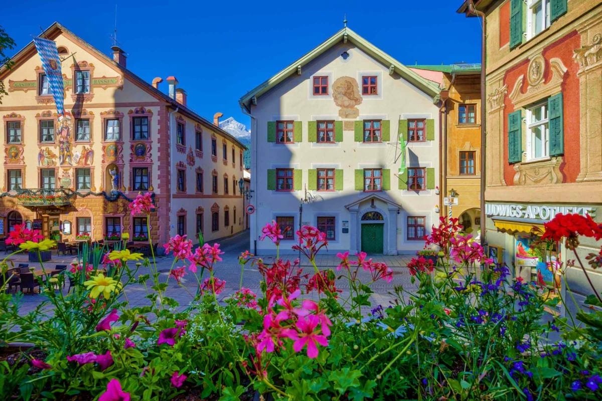 Colorful Bavarian buildings surrounding a town square with pink and purple flowers in foreground, Mittenwald Germany