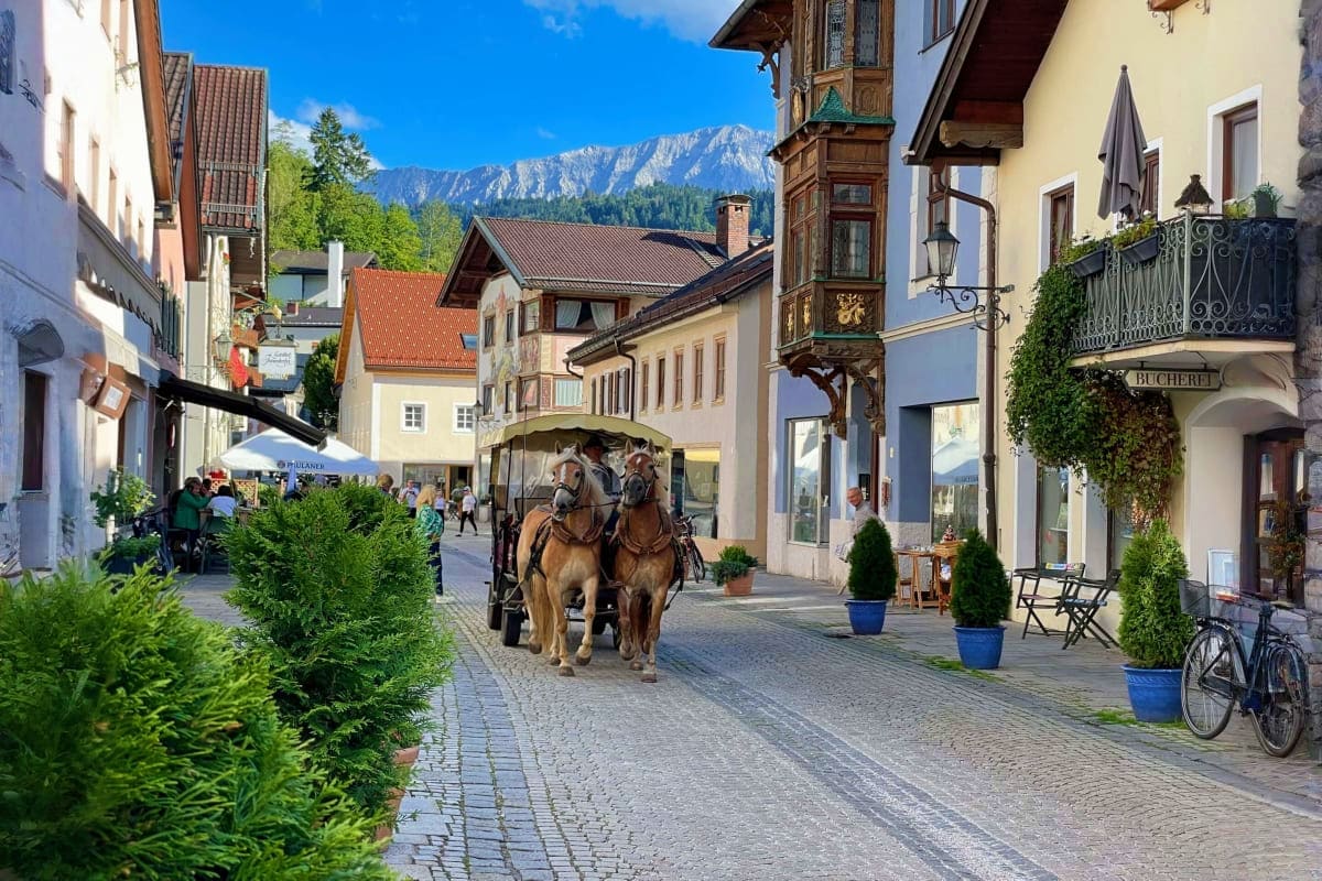 Zugspitze Mountain and Garmisch Day Tour from Munich Horse-drawn carriage on cobblestone street in Garmisch-Partenkirchen with Alpine mountains in background