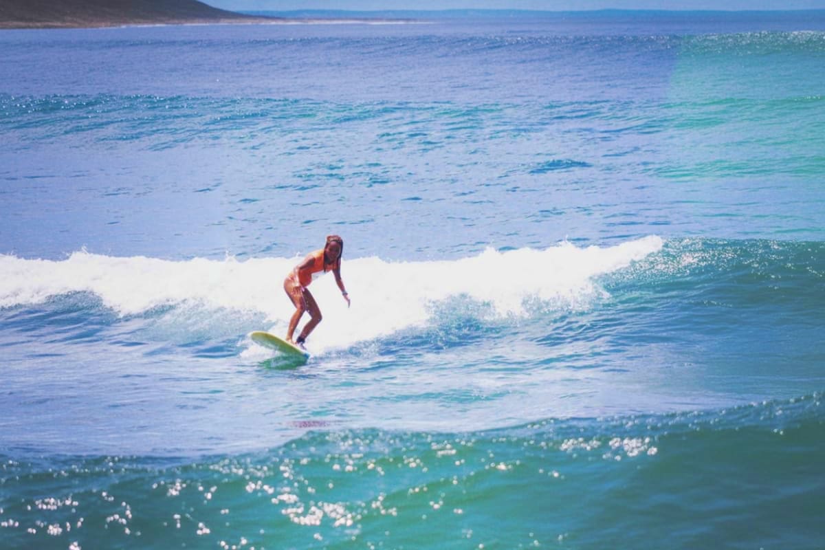 Female surfer riding a wave on a green surfboard at Kuta Beach with white-capped ocean waves and coastline in background