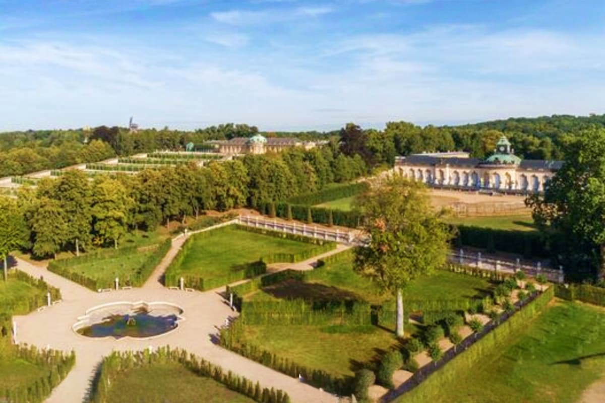 Aerial view of Sanssouci Palace gardens and grounds in Potsdam with manicured lawns, fountain, tree-lined paths, and baroque