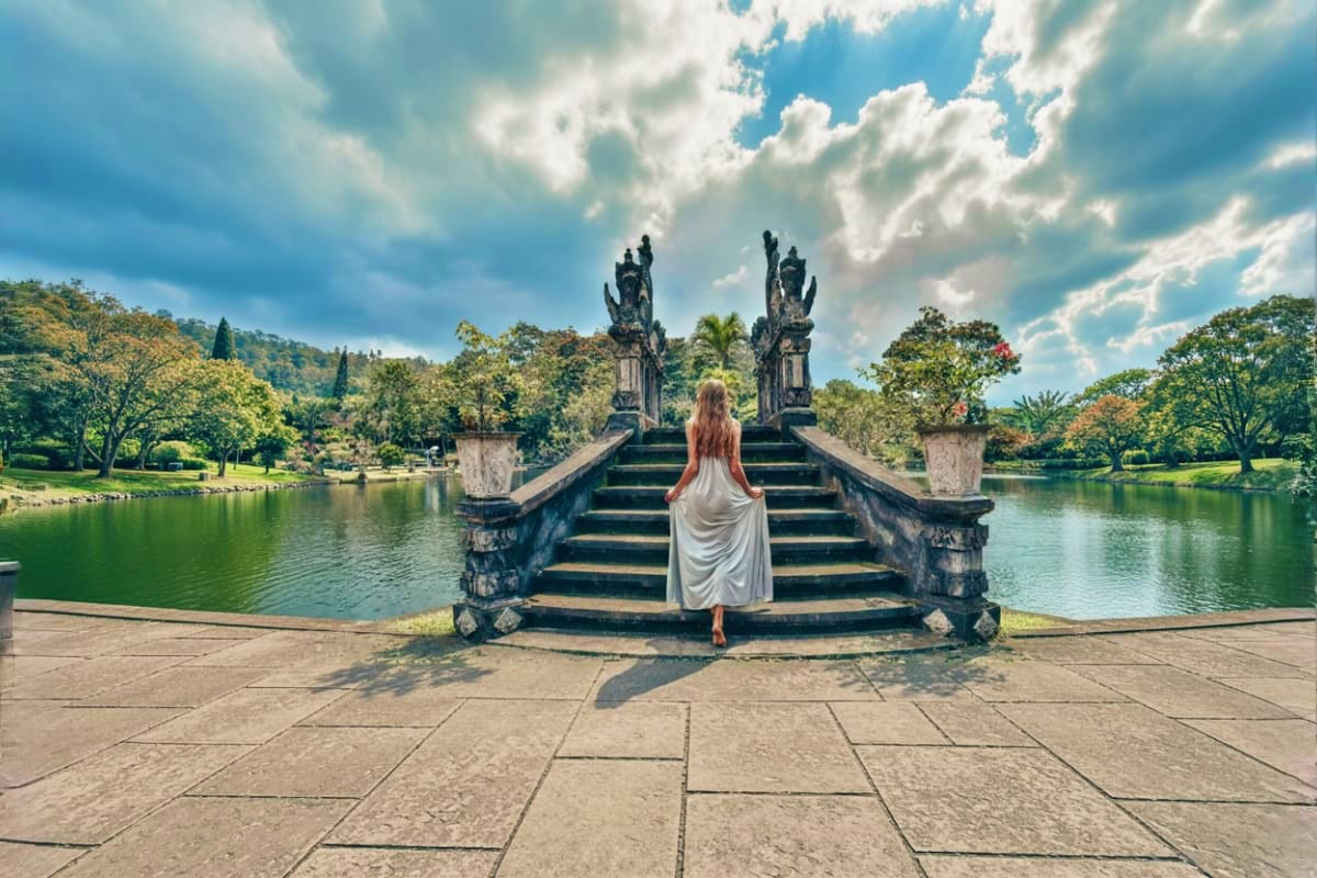 Lempuyang Gate of Heaven Tour Through Bali Most Famous Destinations Woman in white dress ascending ornate stone staircase with dragon statues flanking steps leading to temple gate overlooking s