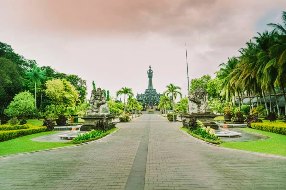 Symmetrical pathway in Bali temple gardens with stone lion statues, palm trees, and ornate tower in the distance
