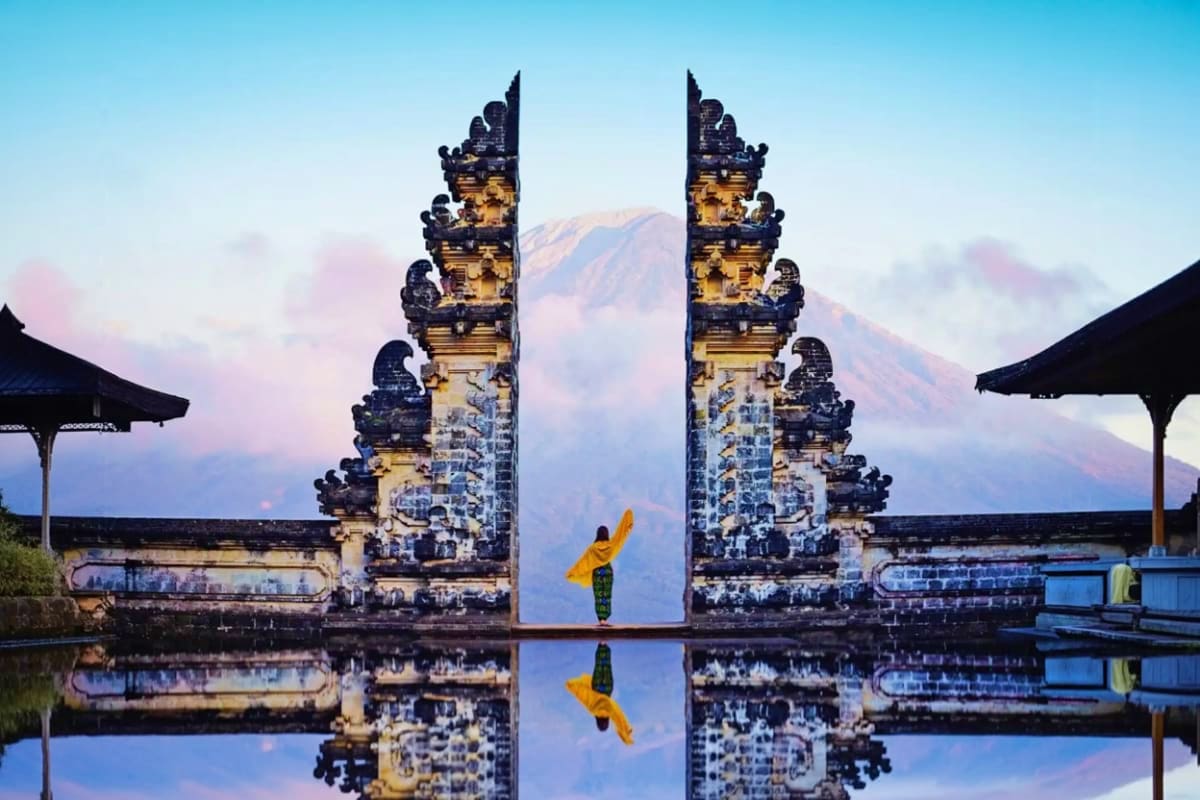Bali Full Day Private Tour Person in yellow jacket standing at ornate Balinese stone gates with mountain view and water reflection