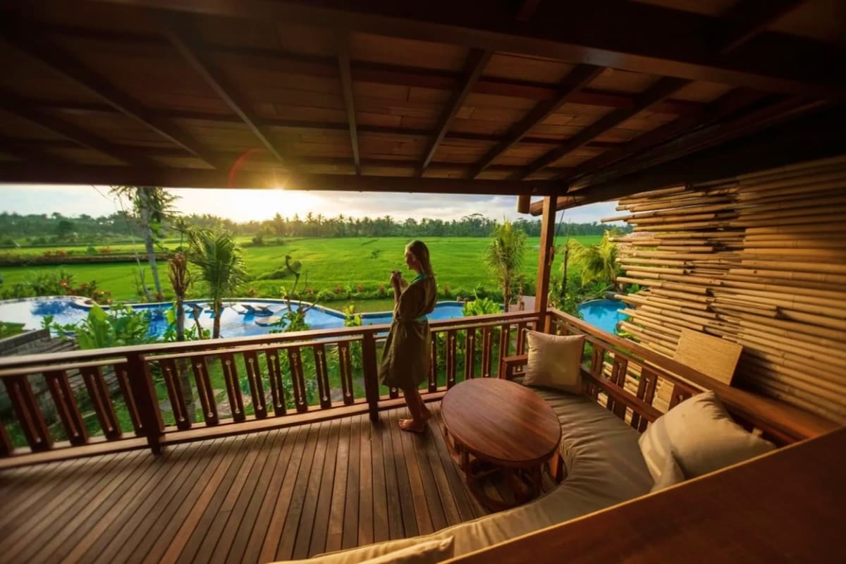 Woman standing on wooden deck overlooking rice fields and blue pool at Bee Cafe Ubud Bali