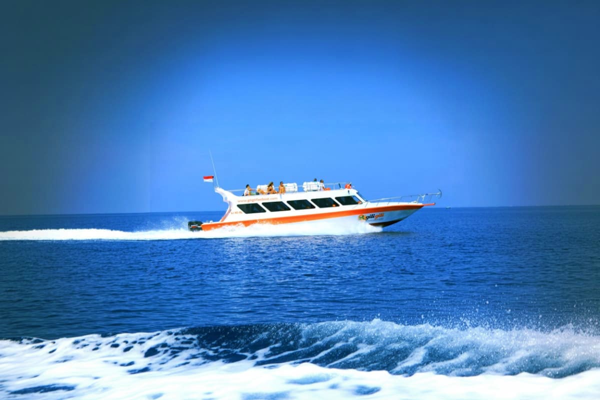 Fast Boat Ticket between Bali Lombok and Nusa with Gili Islands White and orange speedboat with passengers traveling on blue ocean water near a beach with waves
