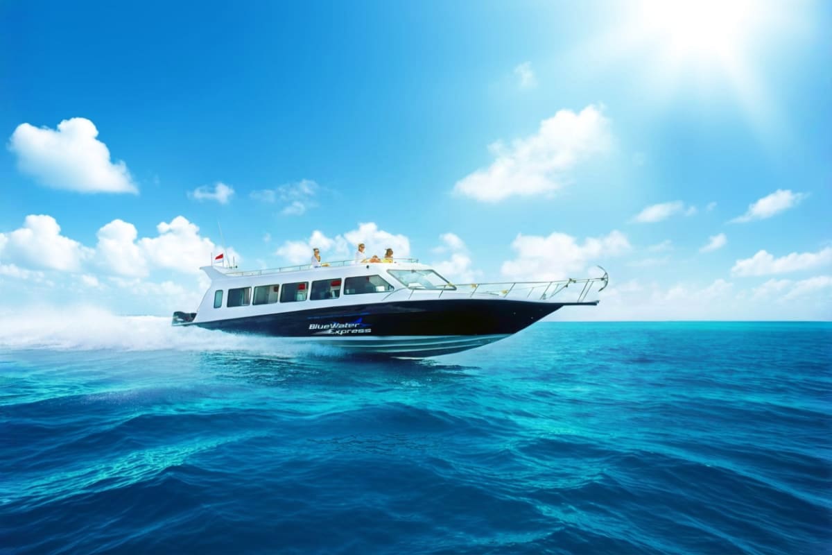 Fast Boat Ticket between Bali Lombok and Nusa with Gili Islands Fast boat with white upper cabin and dark blue hull traveling on turquoise ocean water under clear blue sky with white clouds