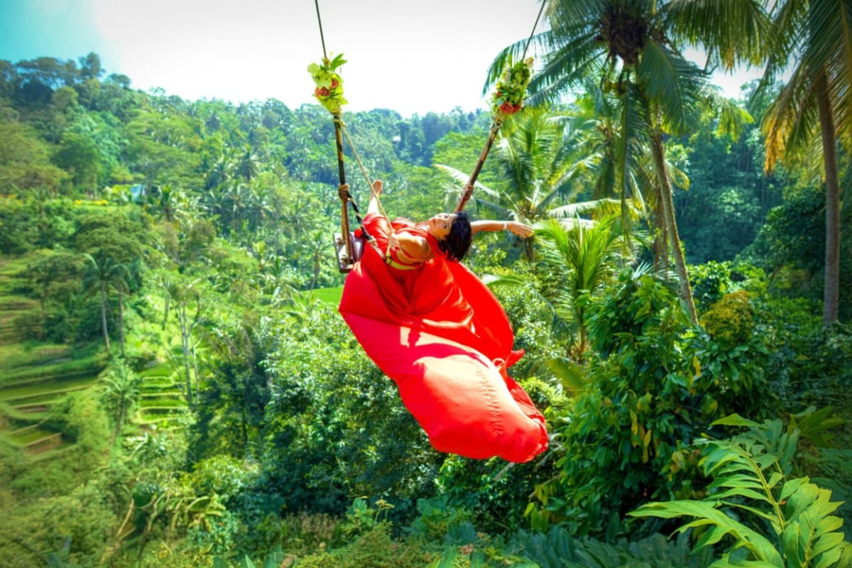 Bali Private Full Day Temple And Waterfall Tour Woman on jungle swing zip line over tropical rainforest canopy in Bali wearing red fabric