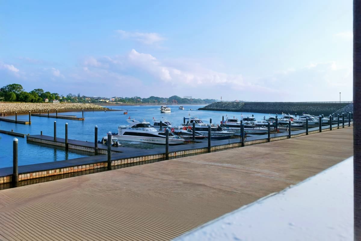 Sanur Harbor with multiple boats moored at wooden docks, blue water, and coastal town visible across the bay