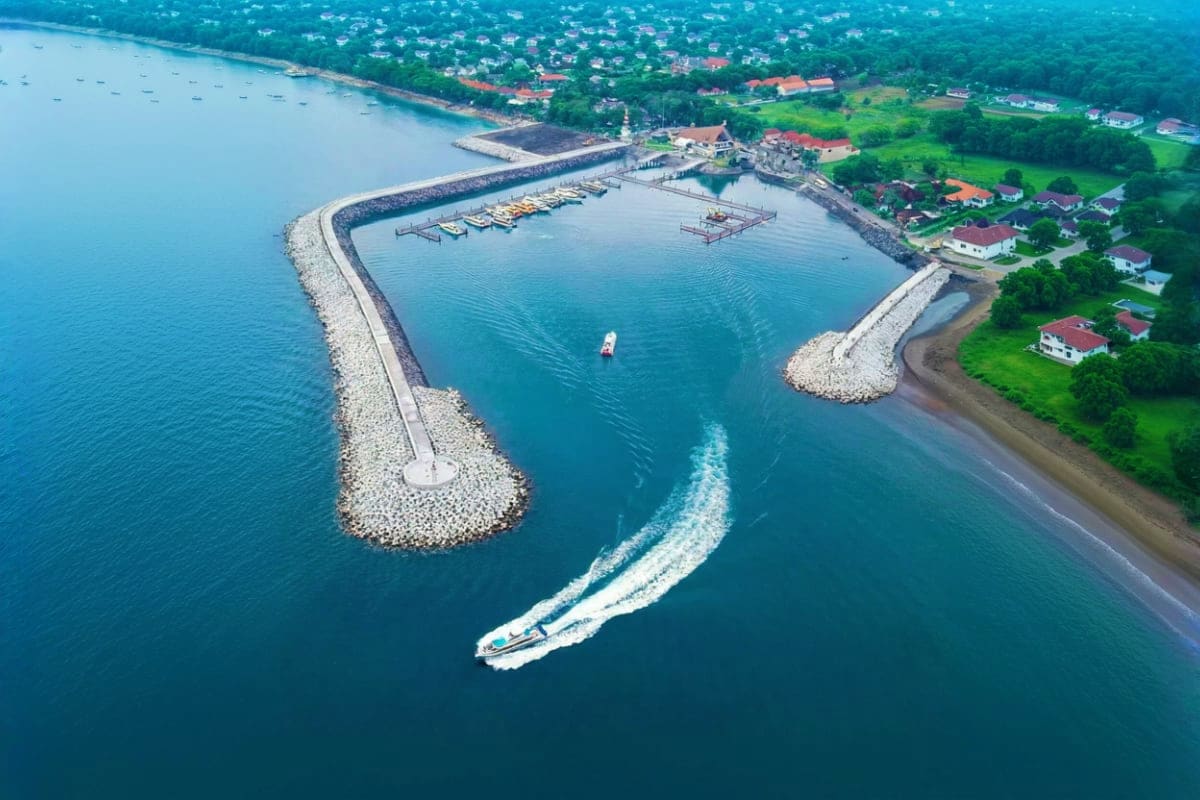 Nusa Penida Day Tour Meet at Sanur Harbor Aerial view of Sanur Harbor with breakwater, moored fishing boats, speedboat approaching, and coastal residential area with g