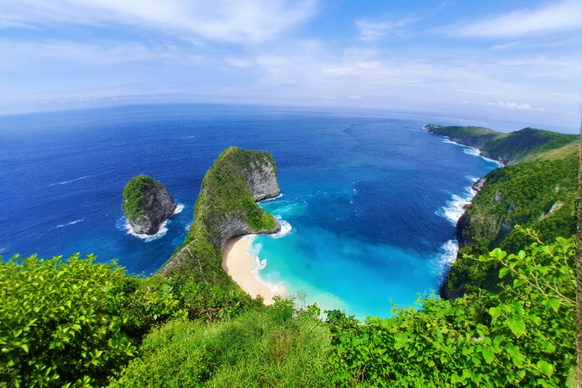 Aerial view of Kelingking Beach in Nusa Penida with turquoise waters, white sand cove, and lush green cliffs
