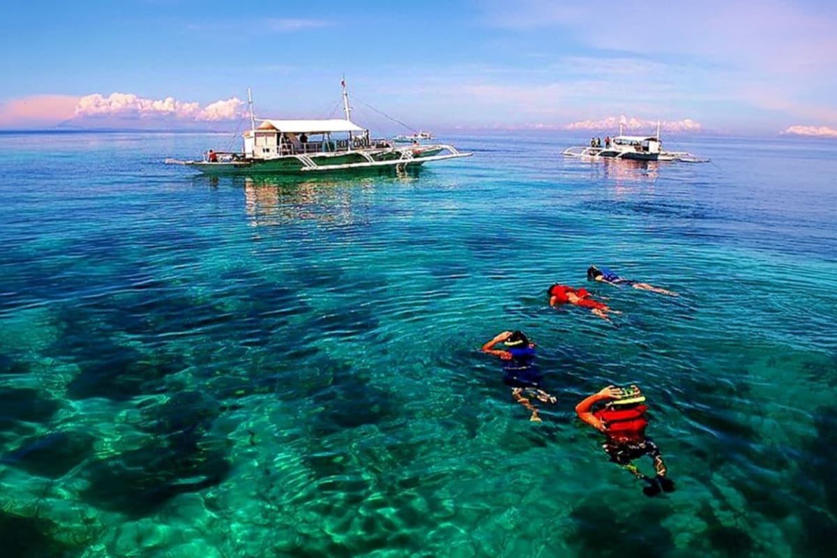 Mactan Water Sports Activities in Cebu Snorkelers in orange life vests swimming in turquoise water near traditional Filipino boats off Mactan Island, Cebu