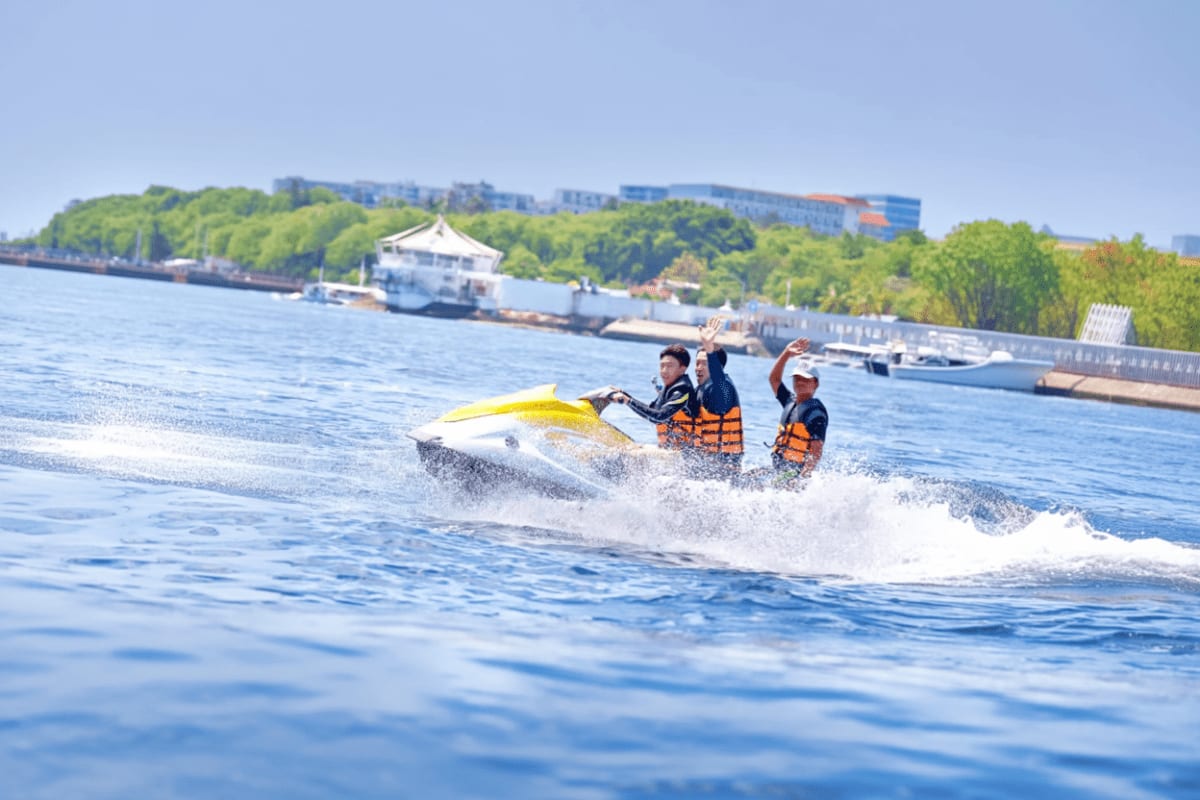 Mactan Water Sports Activities in Cebu Two people on a yellow jet ski riding through ocean waves near a waterfront dock and forested coastline in Cebu
