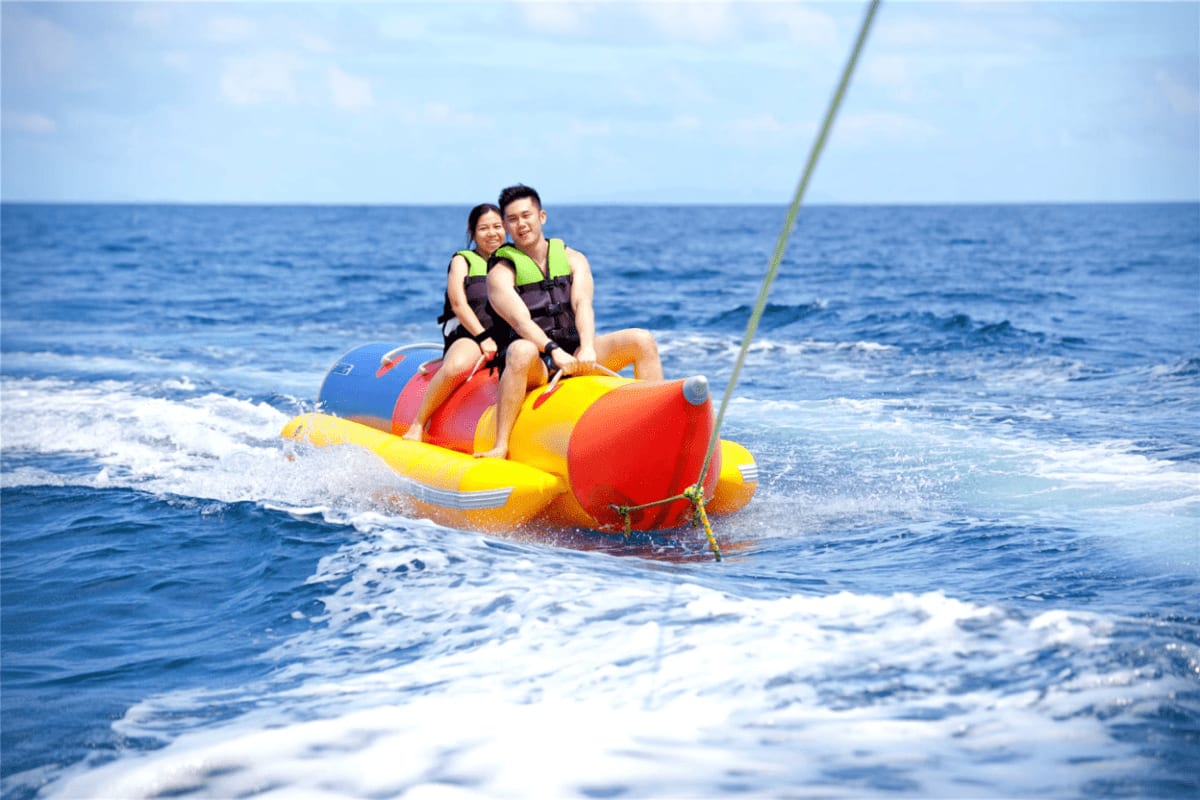 Mactan Water Sports Activities in Cebu Couple riding a colorful inflatable banana boat on ocean waves while wearing yellow life vests in Cebu