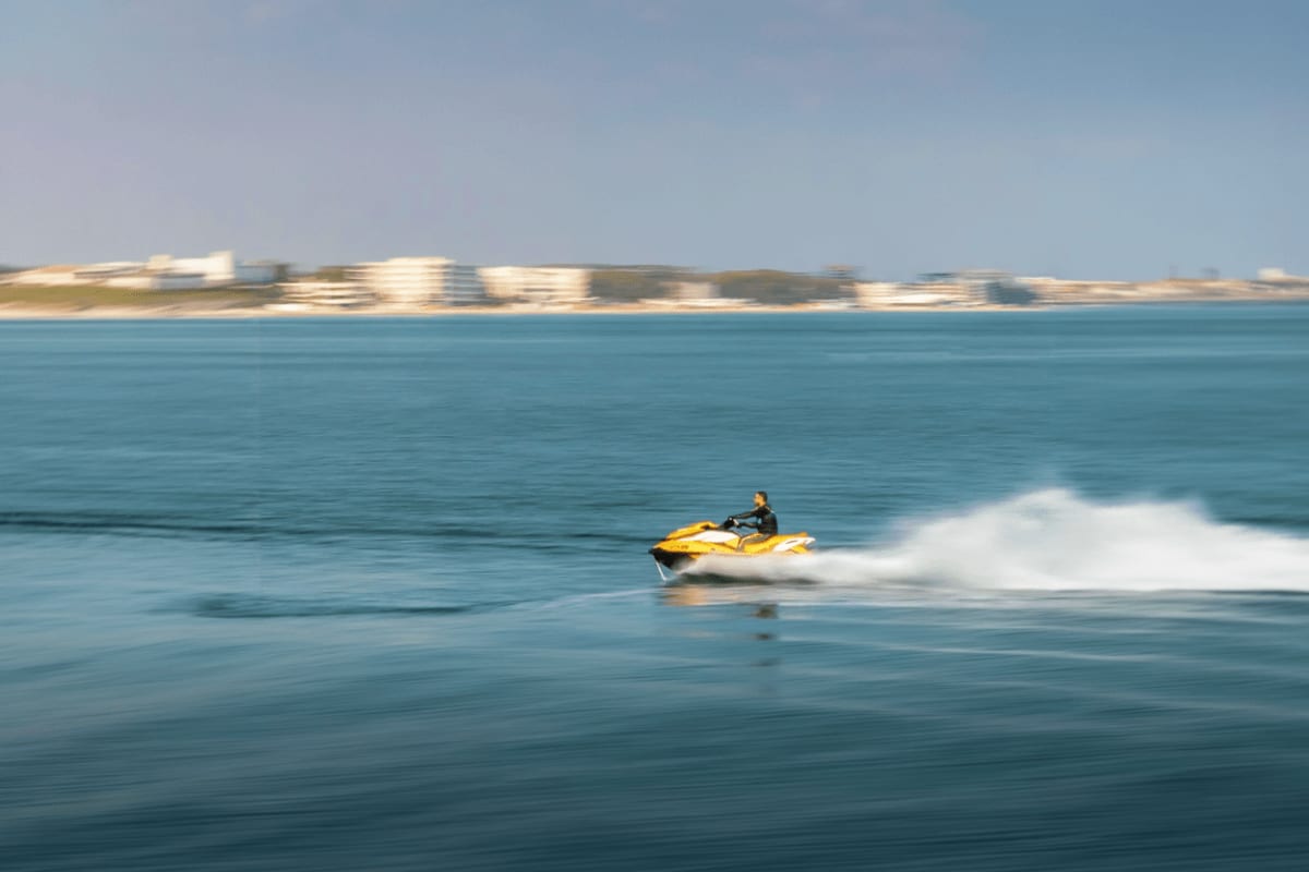 Mactan Water Sports Activities in Cebu Person riding a yellow jet ski in turquoise ocean water with sandy beach and white sand dunes in background, Mactan Cebu