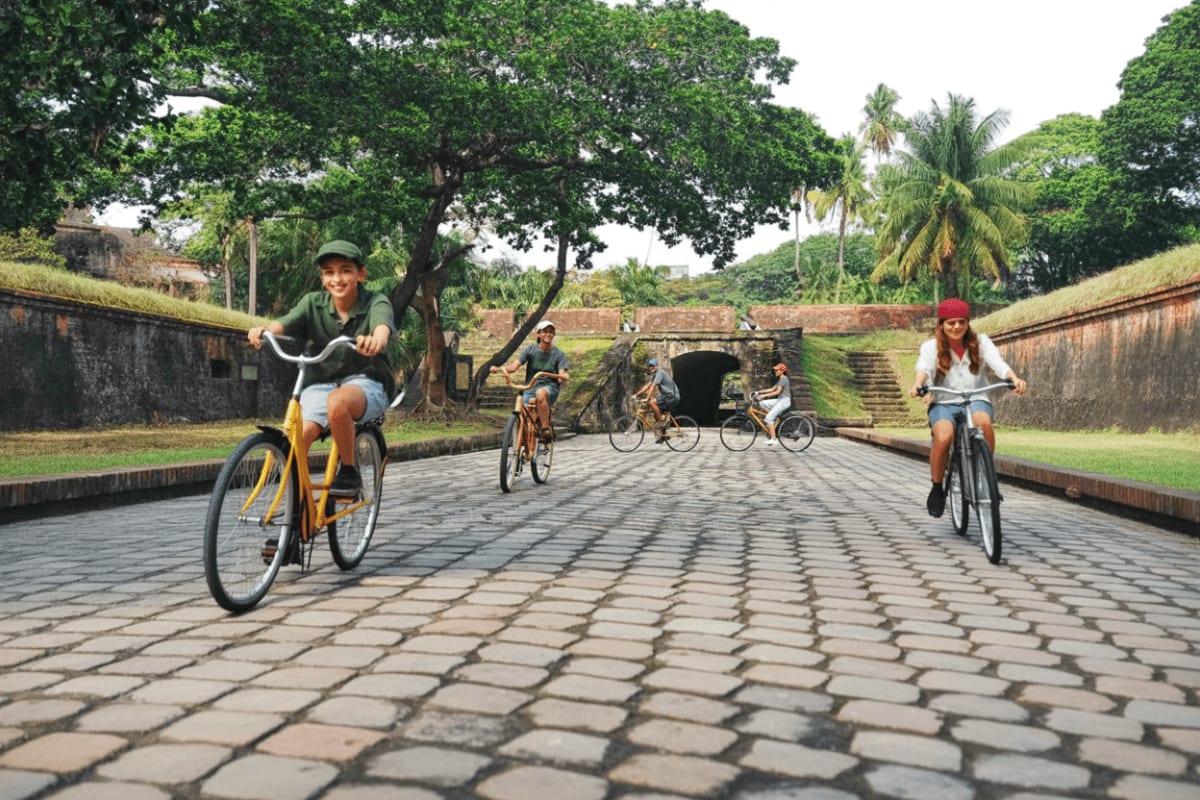 Intramuros Bambike Tour Group of cyclists riding through historic stone-walled fort with palm trees and brick archway tunnel in background