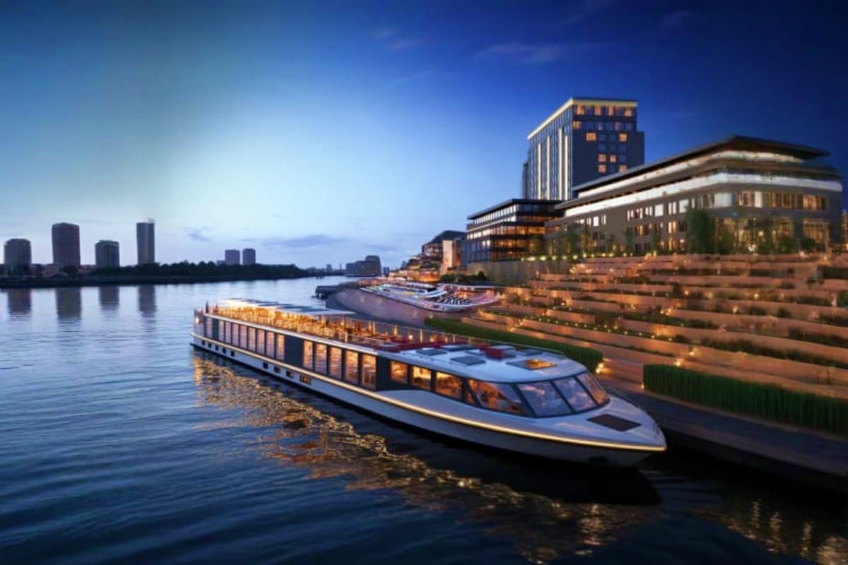 Modern river cruise ship docked at illuminated waterfront promenade with city skyline and high-rise buildings at dusk
