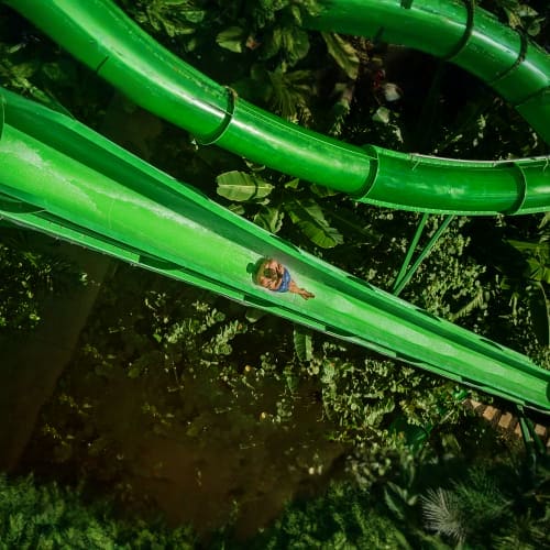 Aerial view of bright green water slides winding through lush tropical vegetation at Waterbom Bali water park