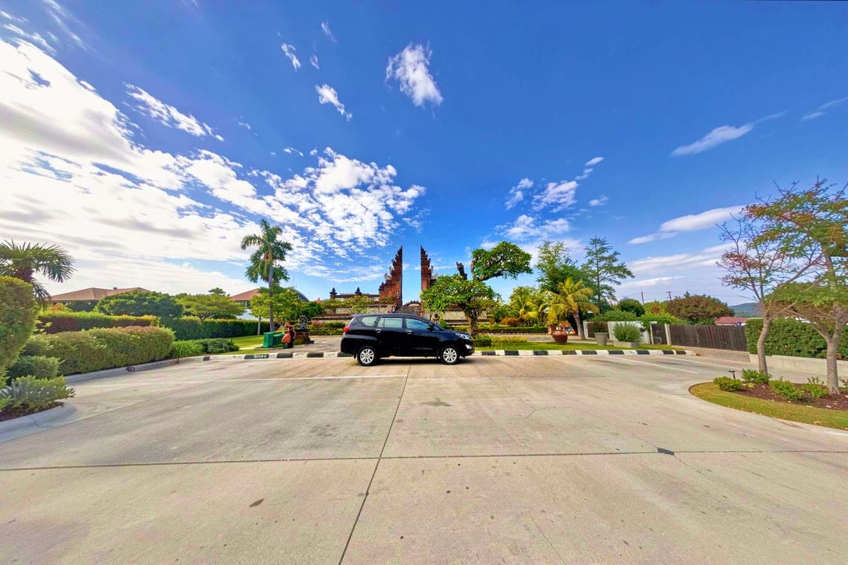 Private Intracity transfers Black car parked at gated entrance with traditional Balinese temple gates and tropical gardens under blue sky
