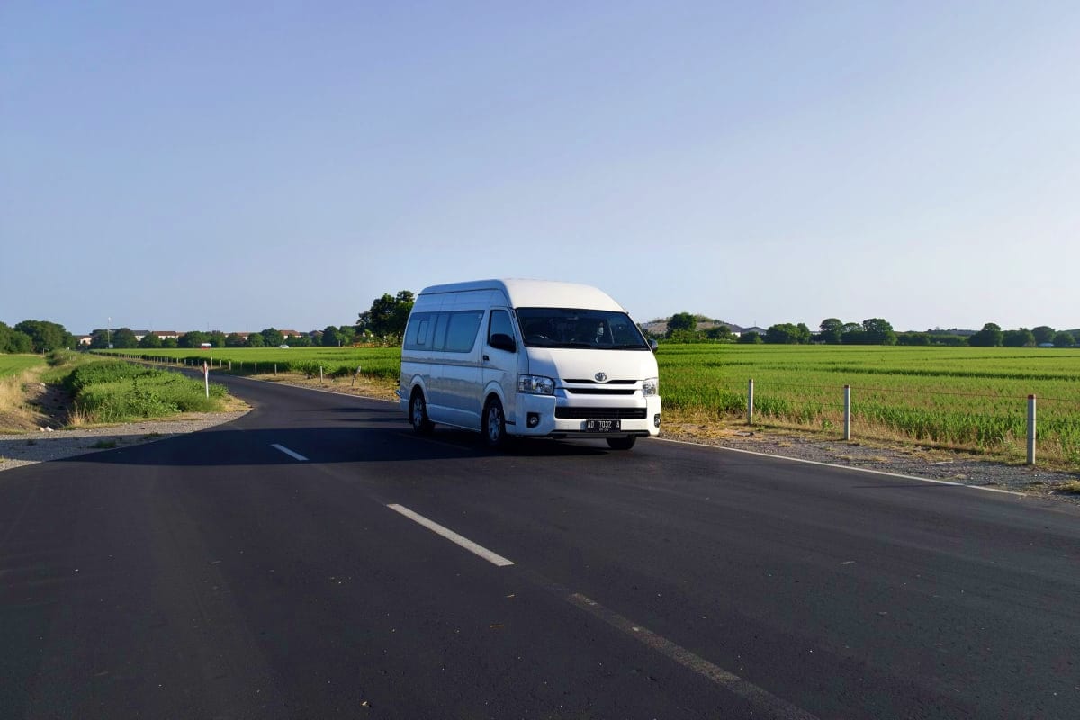 Private Intracity transfers White Toyota minivan parked on rural highway surrounded by green fields and clear sky