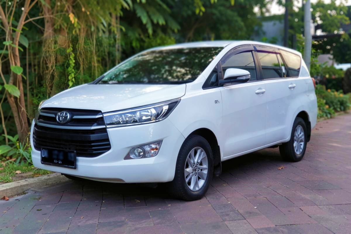 Private Intracity transfers White Toyota Innova minivan parked on brick driveway with lush green foliage in background for private one-way transfer servi
