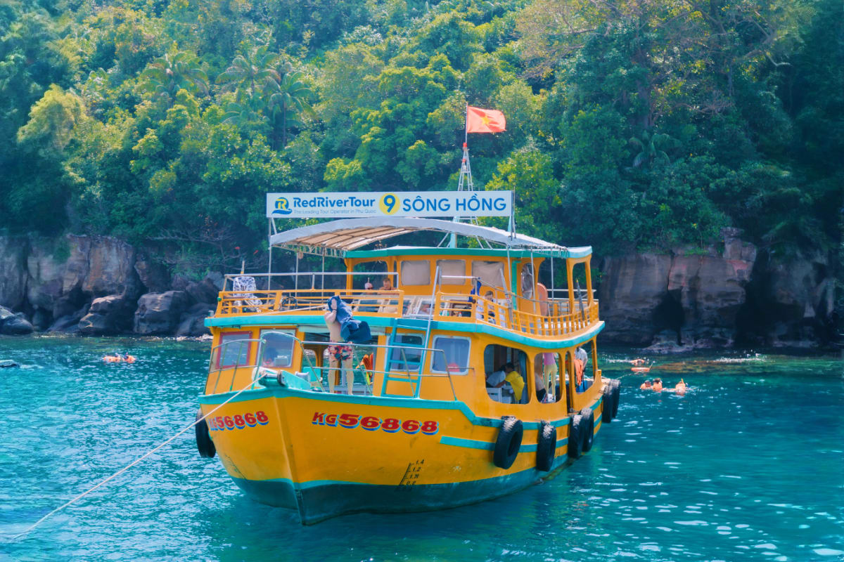 Yellow and blue tour boat with Vietnamese flag anchored in turquoise water near limestone cliffs and dense forest